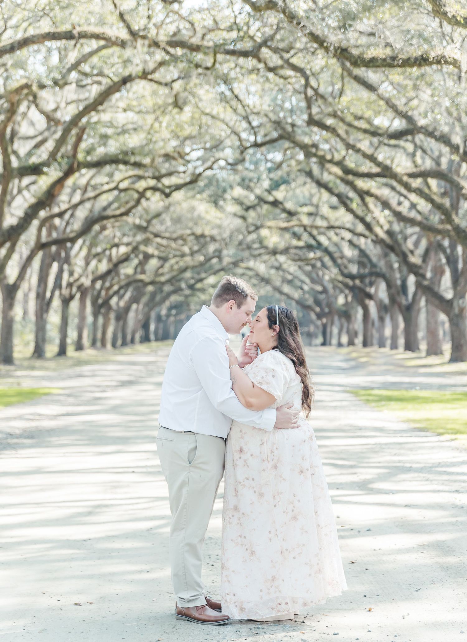 Couple sharing a kiss on a beautiful tree-lined path during their engagement session.