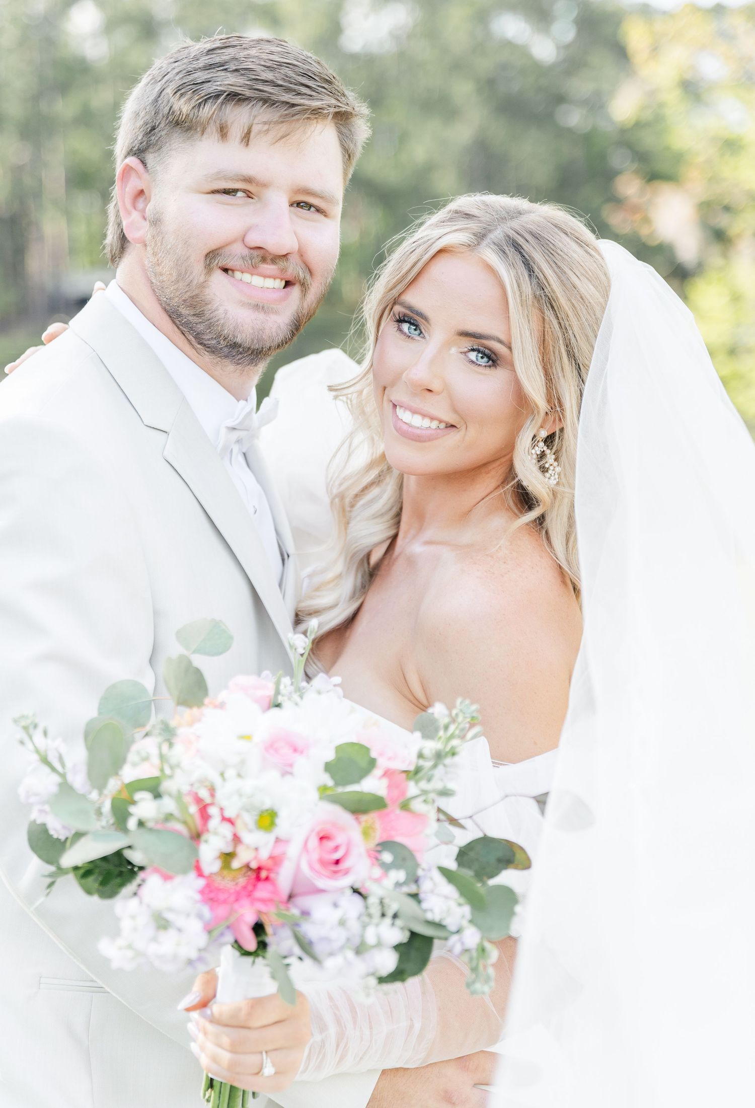Joyful wedding portrait of newlyweds smiling at camera with bride holding pink and eucalyptus bouquet.