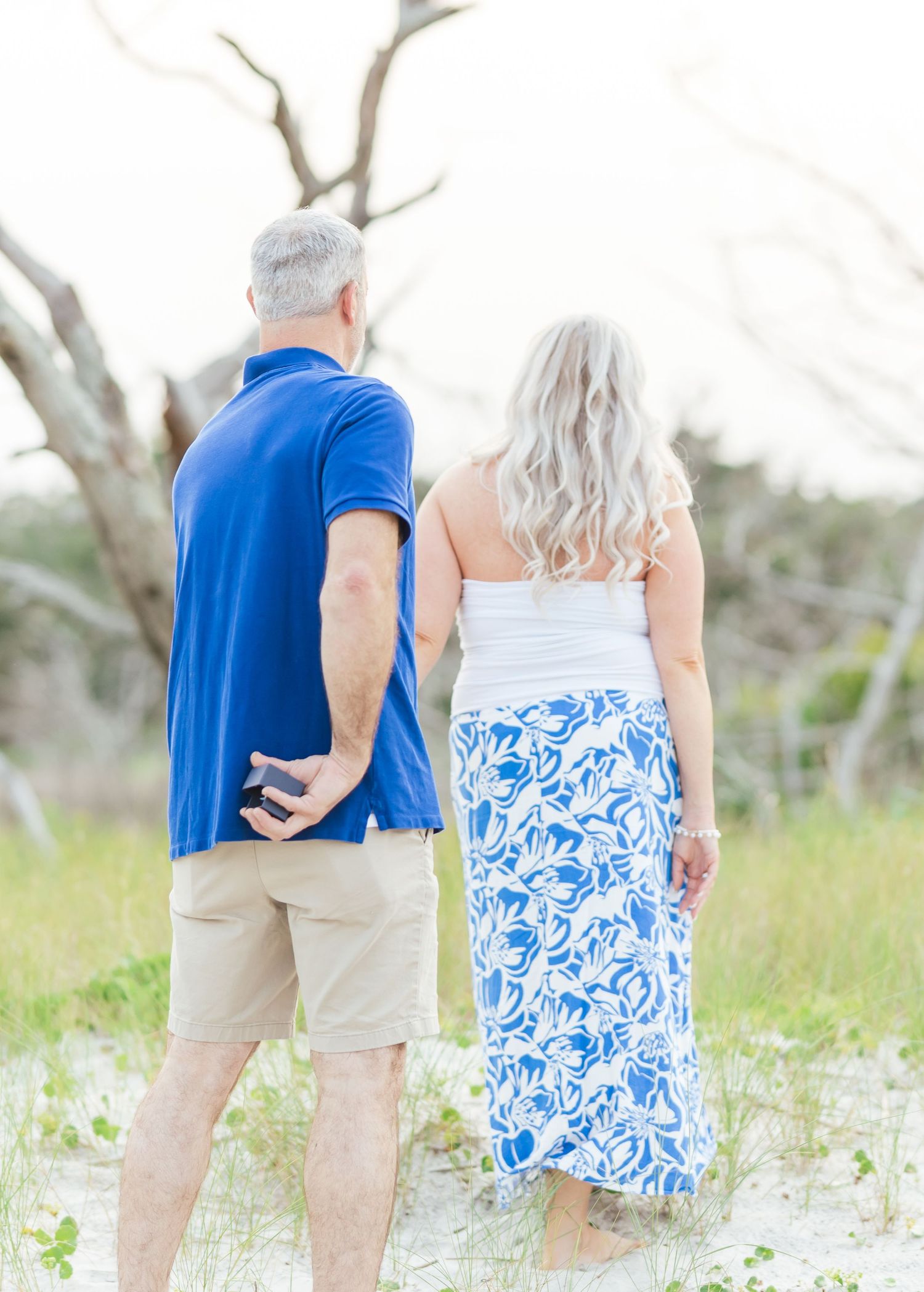 Couple in matching blue and white outfits walking along sandy beach path with driftwood.