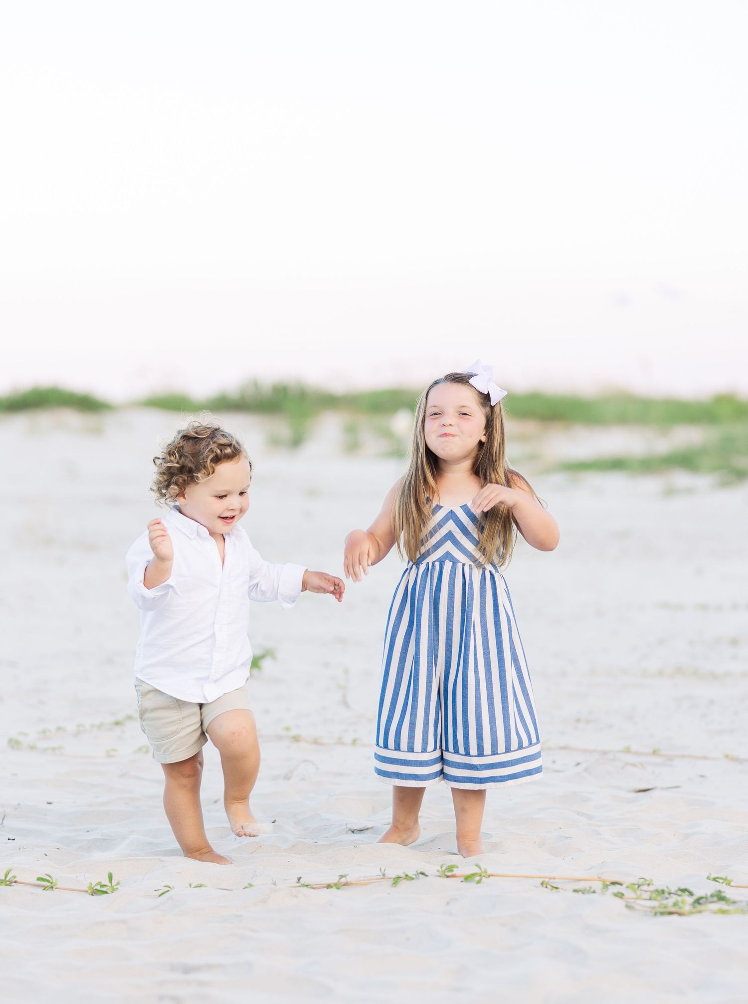 Two children playing together on a sandy beach, one in stripes and one in white.