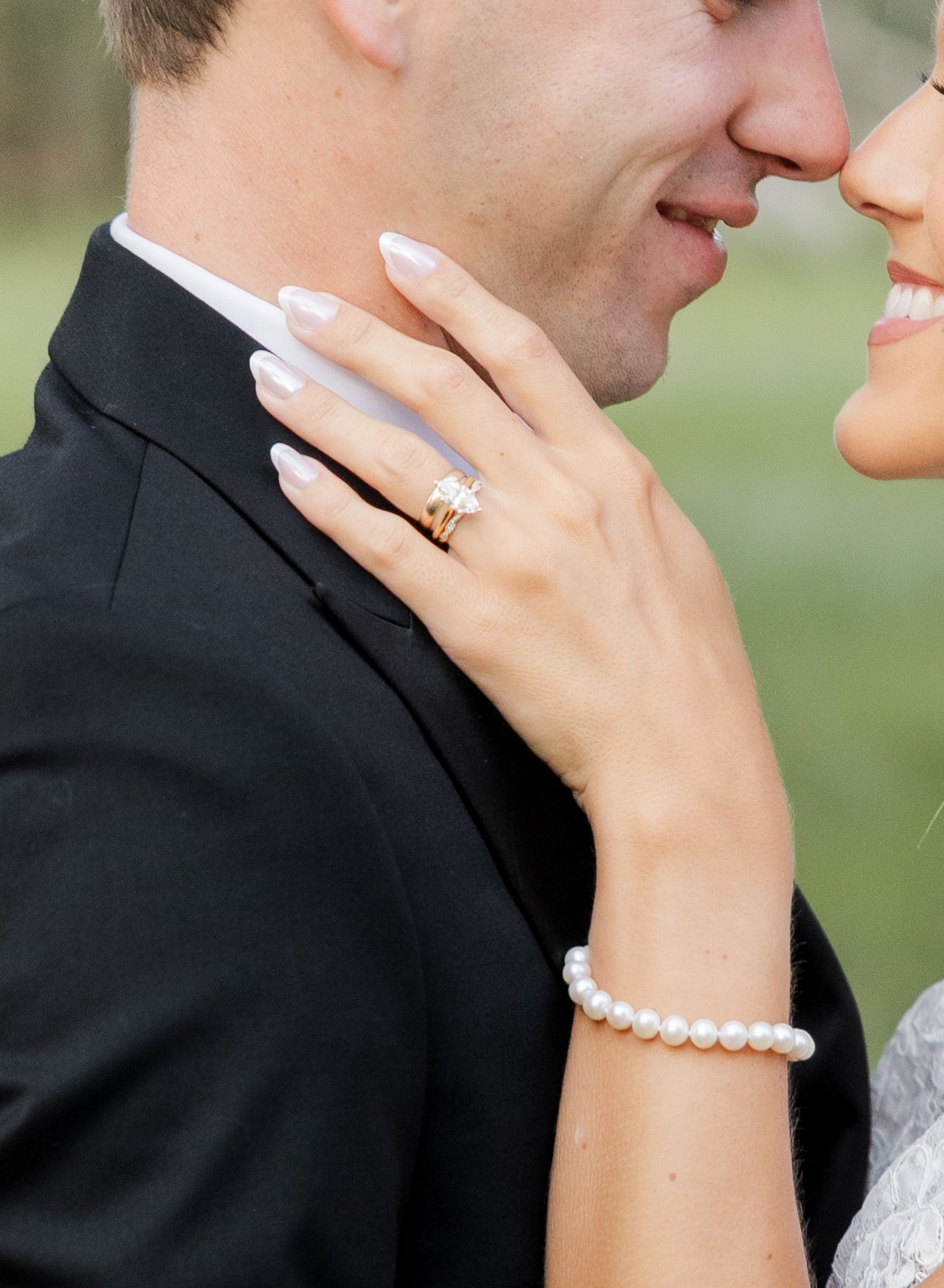 Close-up of a couple embracing, showcasing a diamond engagement ring and pearl bracelet on the bride's hand.