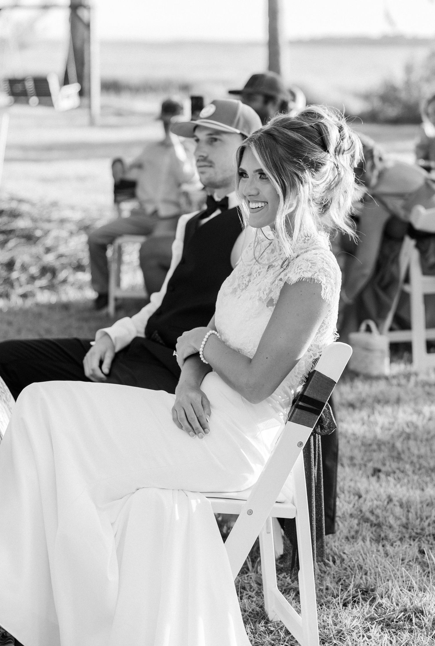 Black and white photo of smiling bride and groom seated at outdoor wedding reception.