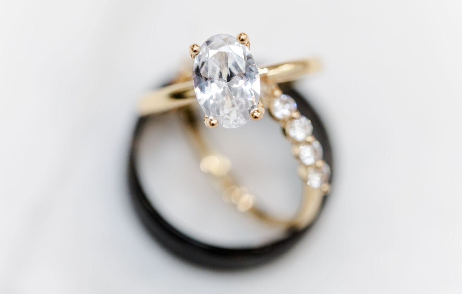 A gold engagement ring with a pear-shaped diamond and small accent stones showcased against a dark wedding band.