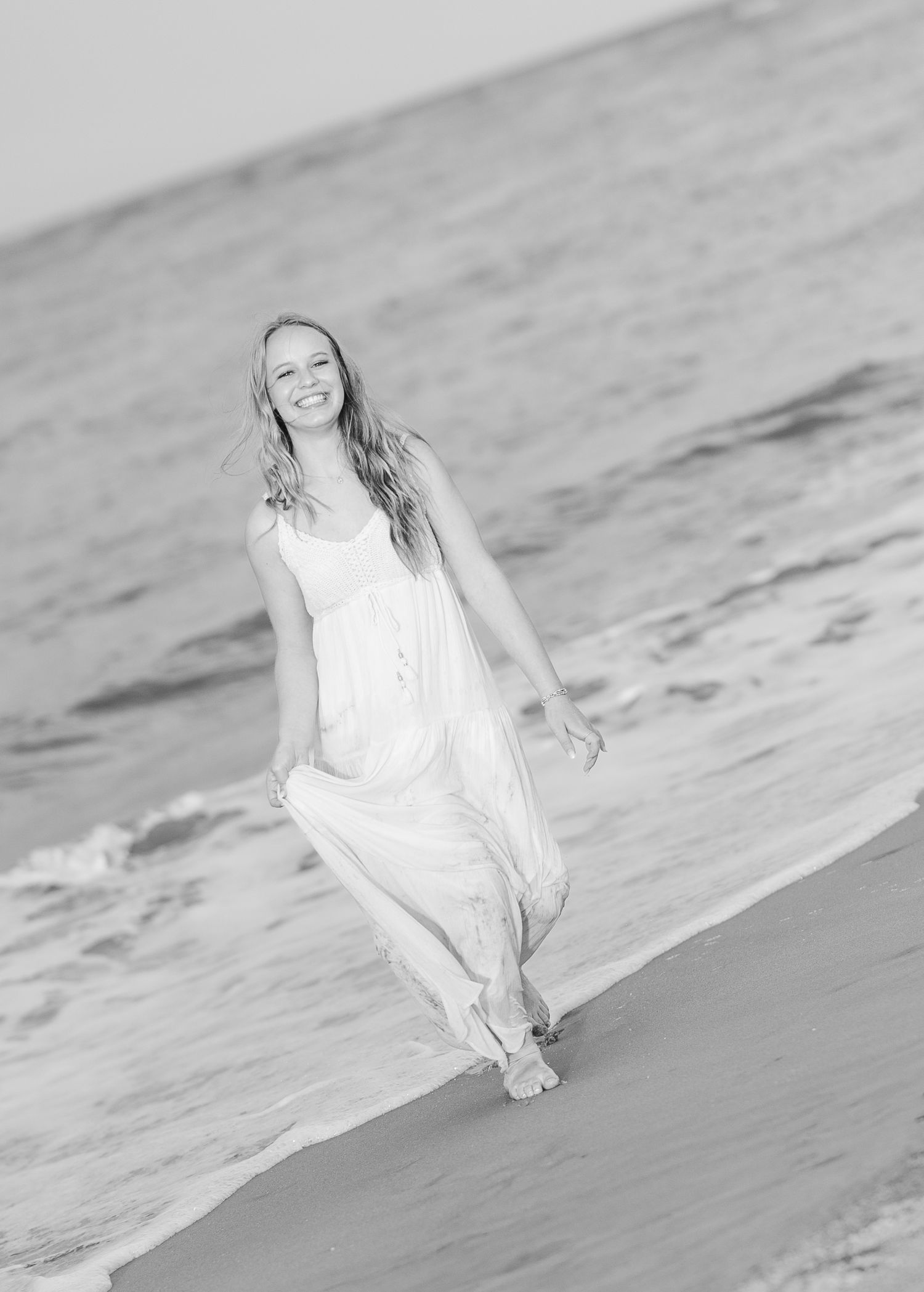 A serene beach scene in black and white with someone in a flowing white dress sitting by the ocean waves.