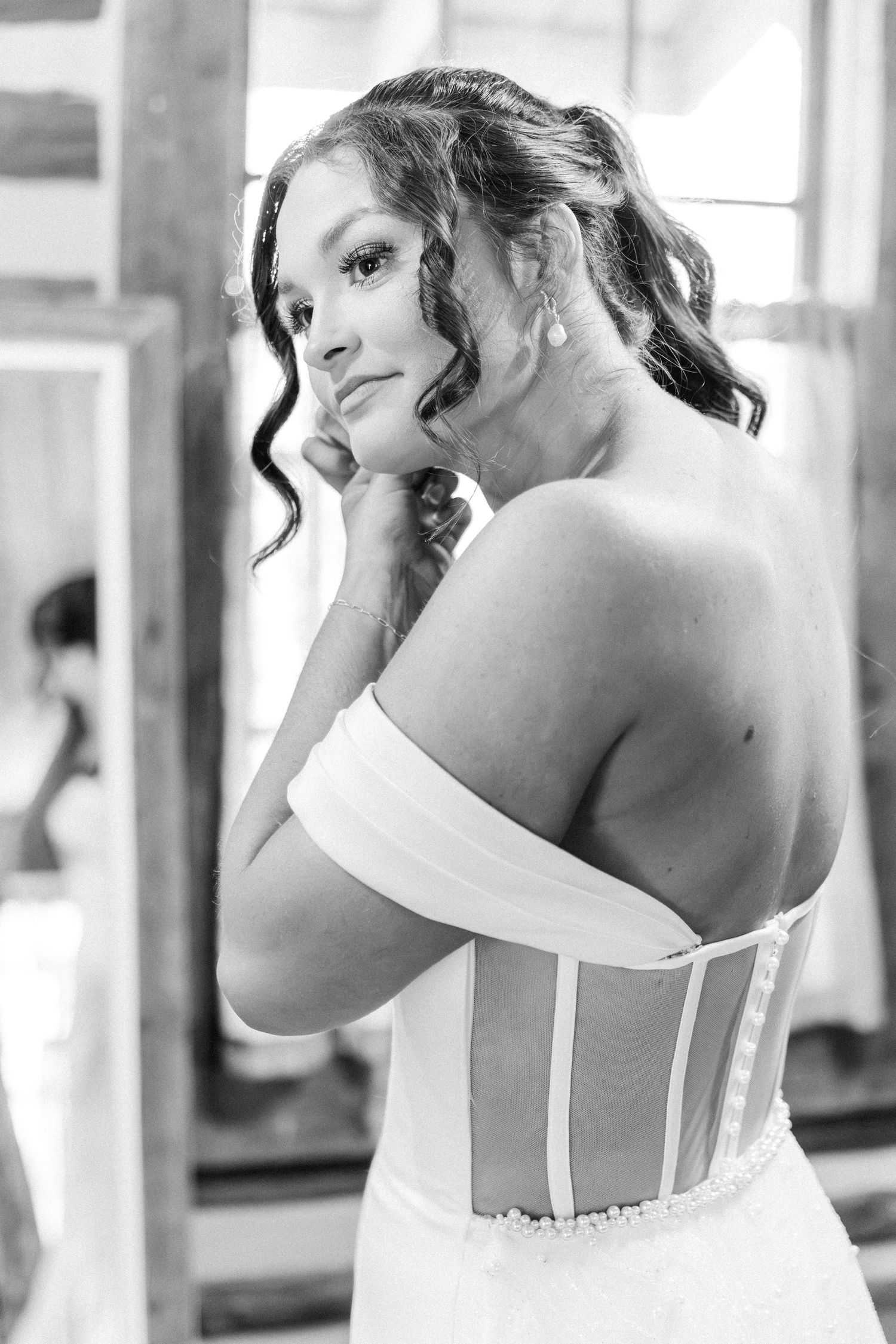 Bride in strapless corset wedding gown poses over shoulder in black and white portrait.