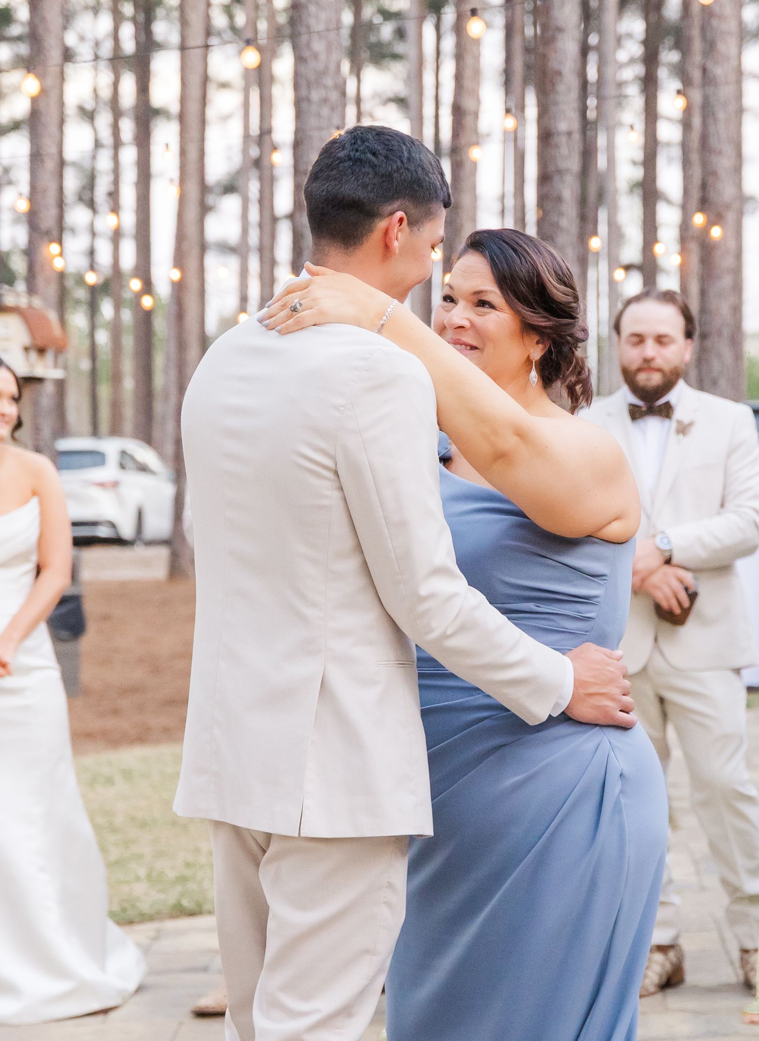 Groom shares a tender mother-son dance outdoors under string lights at a wedding reception.