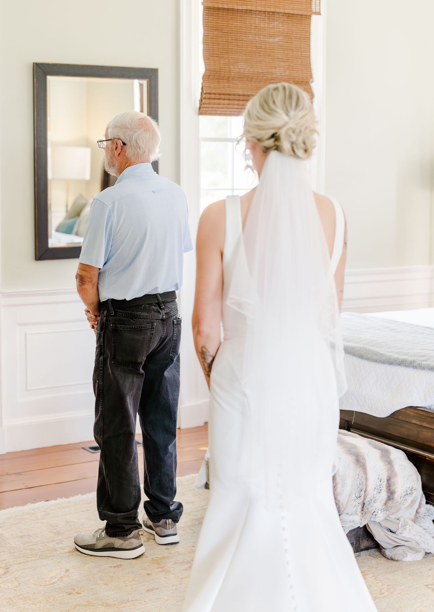 Bride in white gown and veil sharing emotional first look moment with father indoors before wedding.