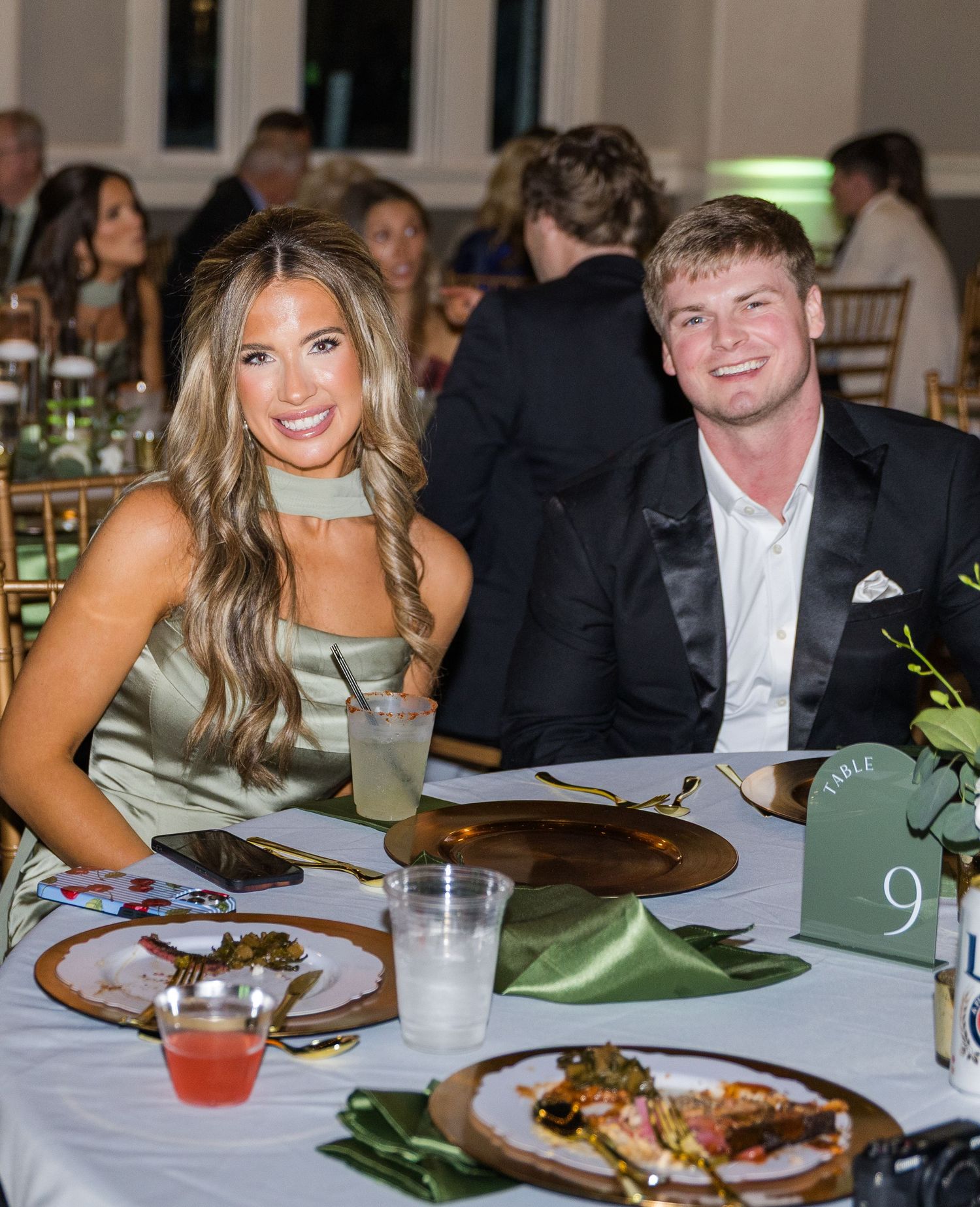 Smiling couple in formal attire seated at table 9 during a wedding reception dinner.