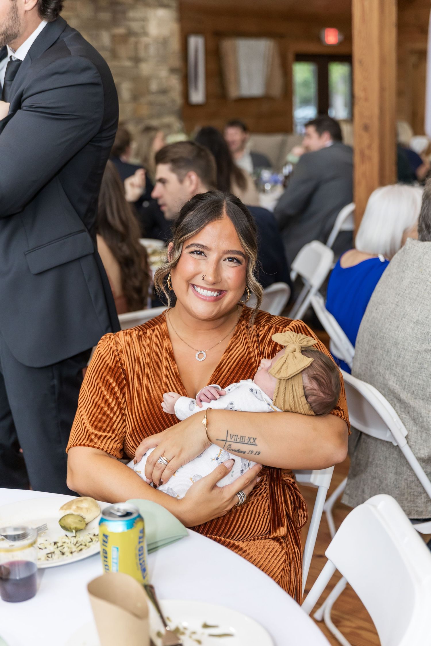 A guest in a rust-colored velvet dress smiles while seated at a table during a formal event.