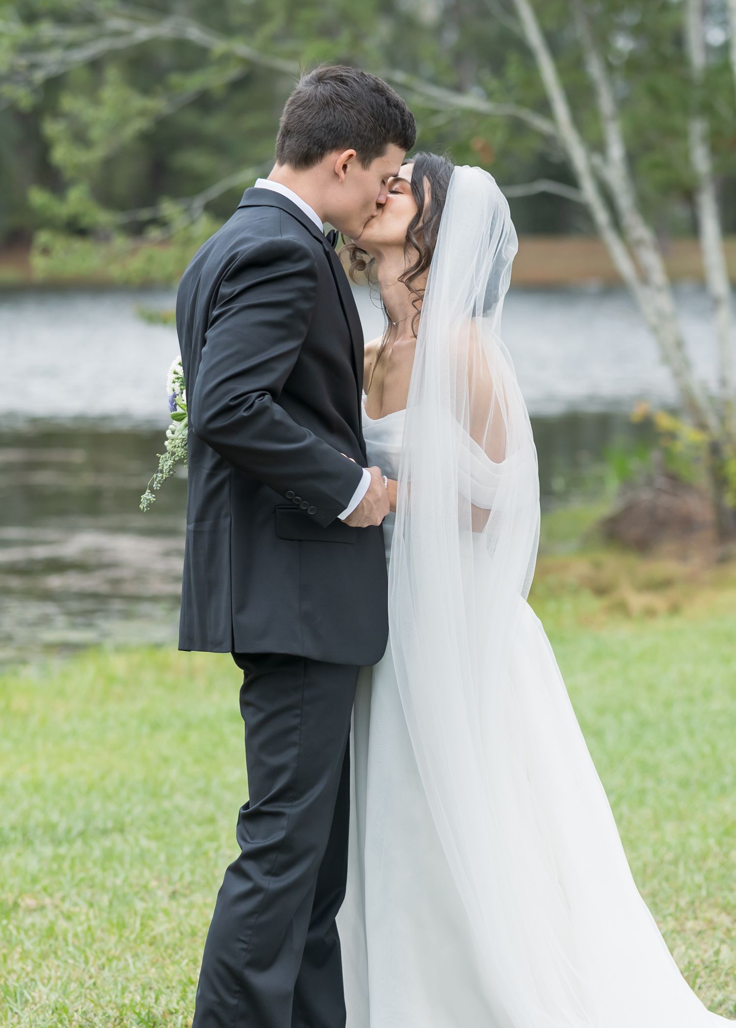 Wedding couple shares intimate moments outdoors by a lake with birch trees in the background.