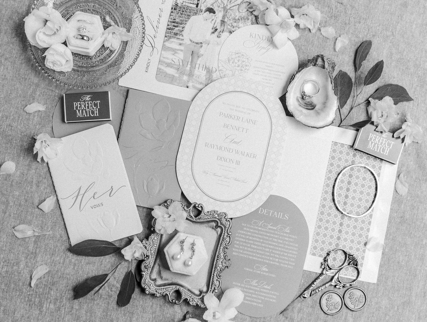 Flatlay of wedding accessories including invitations, perfume bottles, and decorative items arranged in black and white.