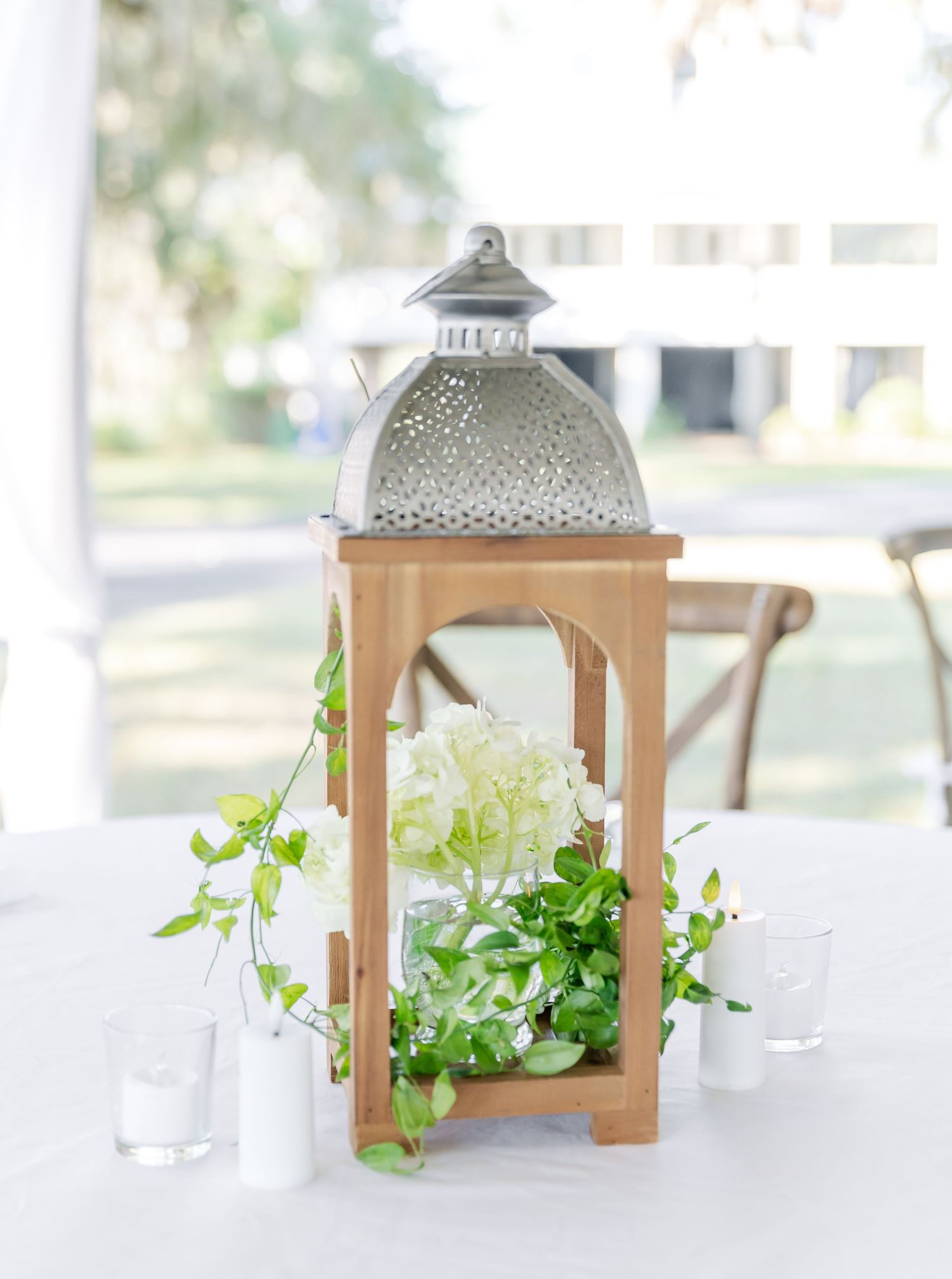 Elegant wooden lanterns with metal tops and greenery decorations arranged on a white surface for wedding decor.