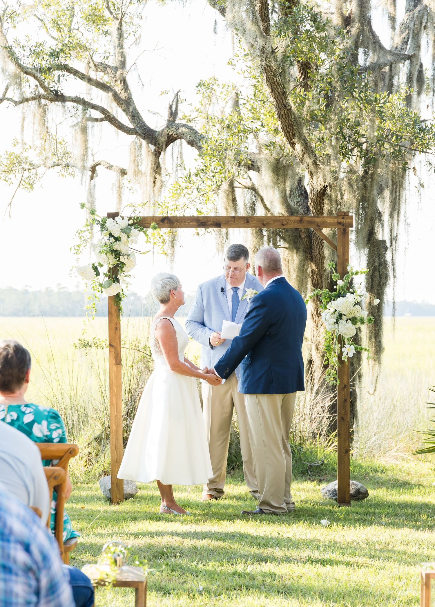 Rustic outdoor wedding ceremony taking place under oak trees draped with Spanish moss.