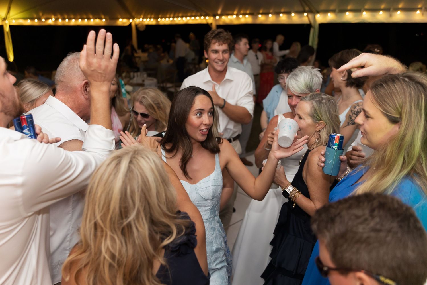 Wedding reception dance floor filled with guests dancing under warm string lights at night.