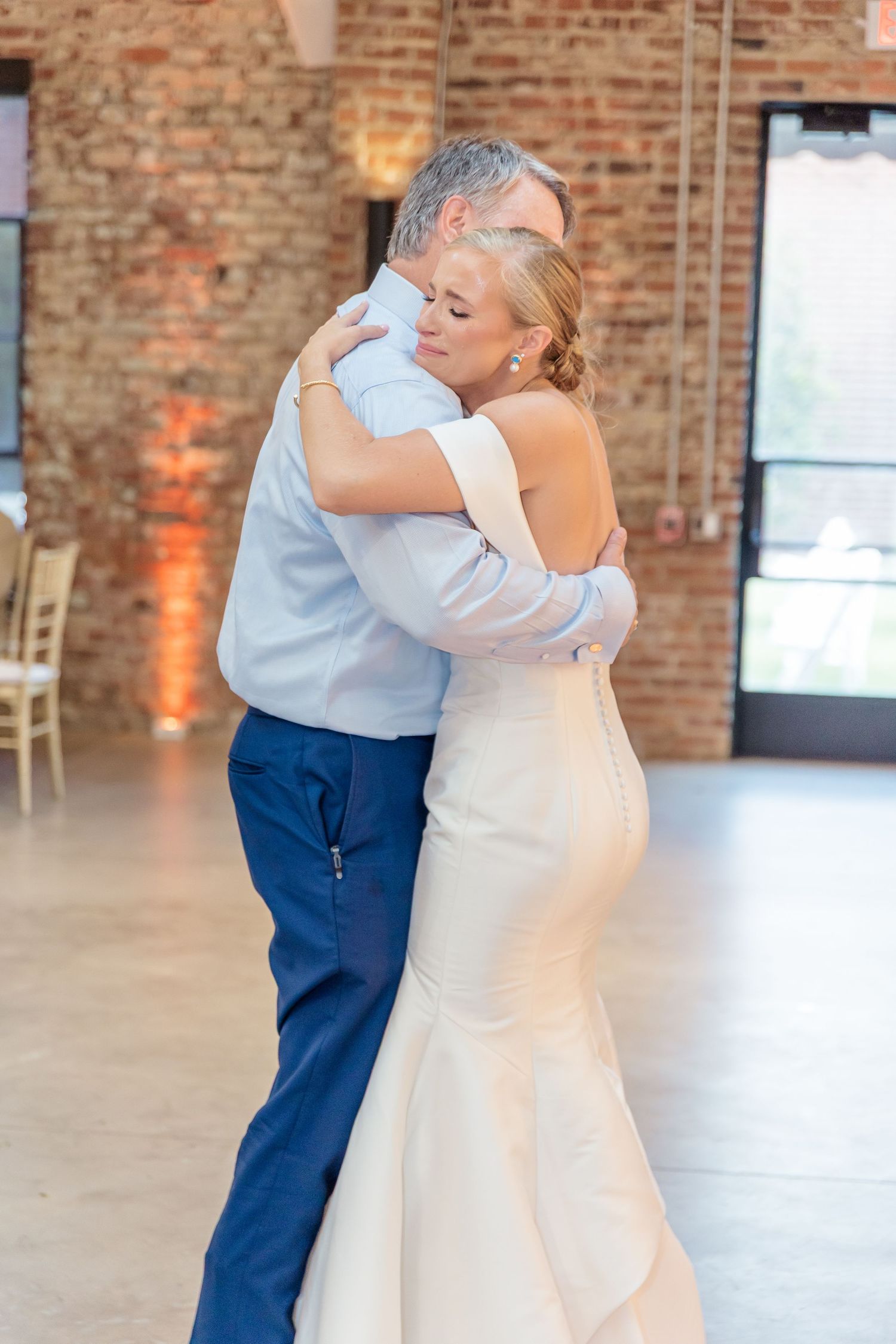 Bride and groom share an intimate dance in an industrial brick venue with romantic amber lighting.