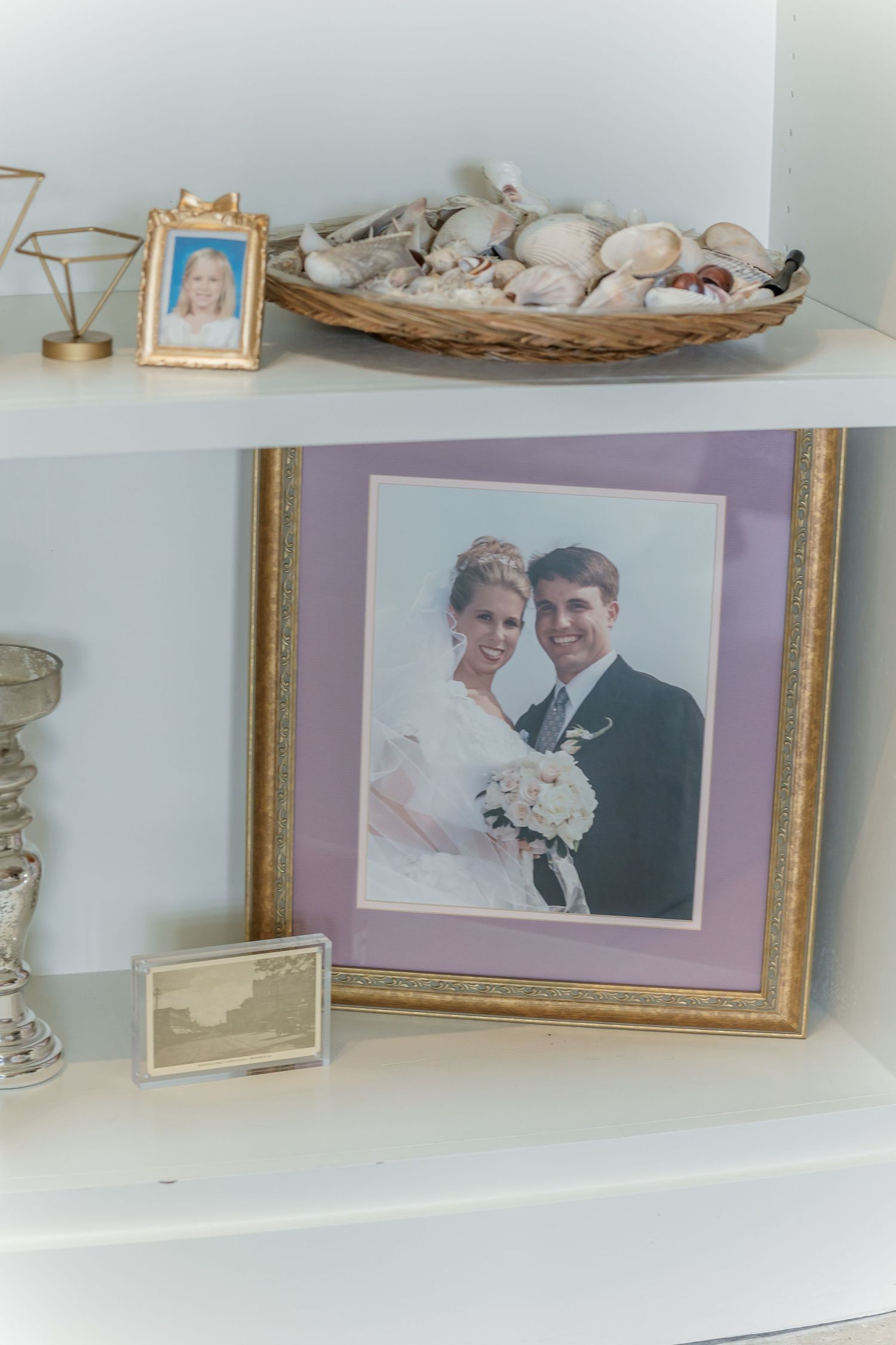 Decorative shelf display with framed photographs and seashells in a woven basket.