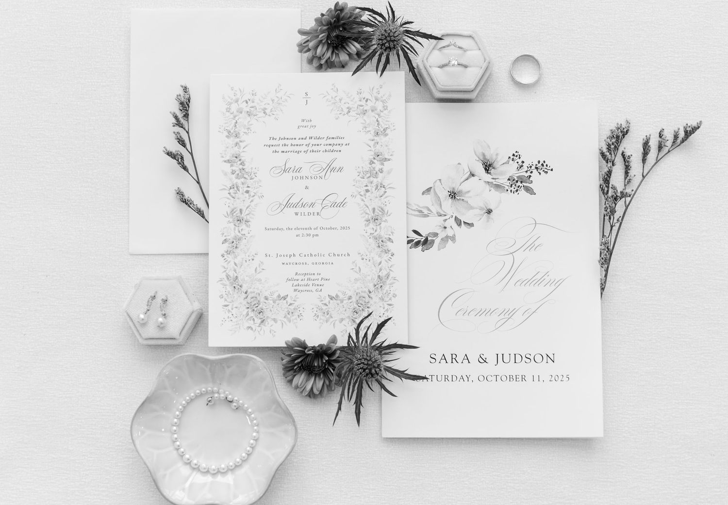 Elegant wedding invitation suite in white with floral designs and calligraphy, styled with delicate foliage and decorative boxes.