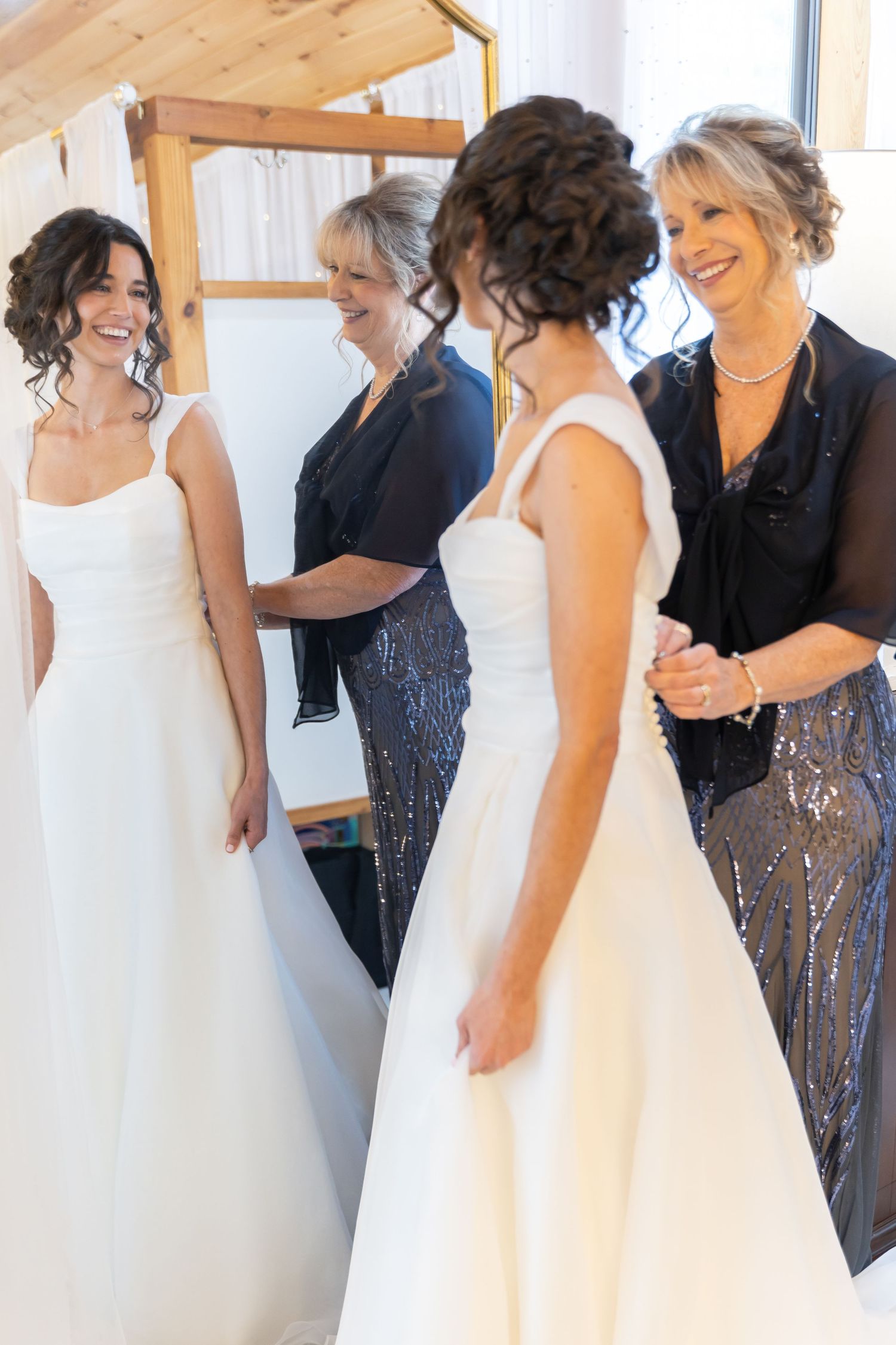 A group of women in formal dresses gather closely together in a bright indoor space.