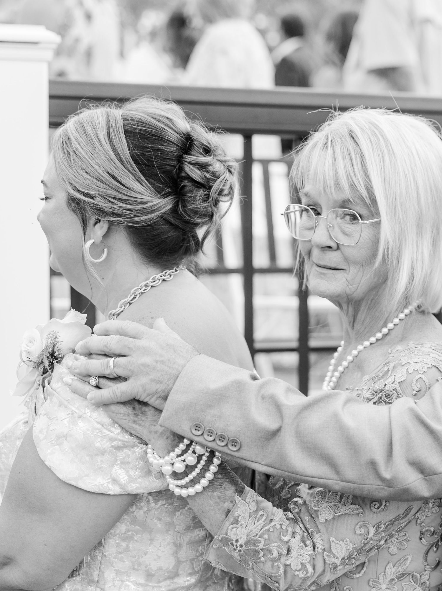 Black and white photo of older woman tenderly placing hands on brides shoulders at wedding venue.