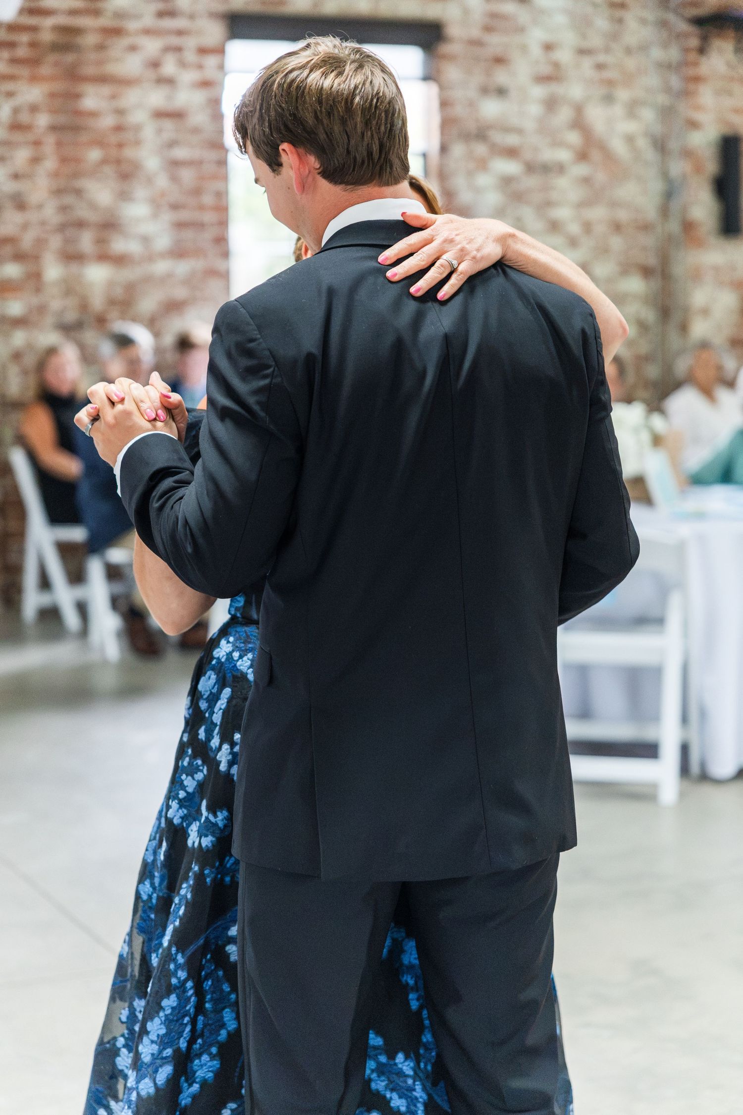 Groom dancing with woman in blue floral dress during wedding reception mother-son dance.
