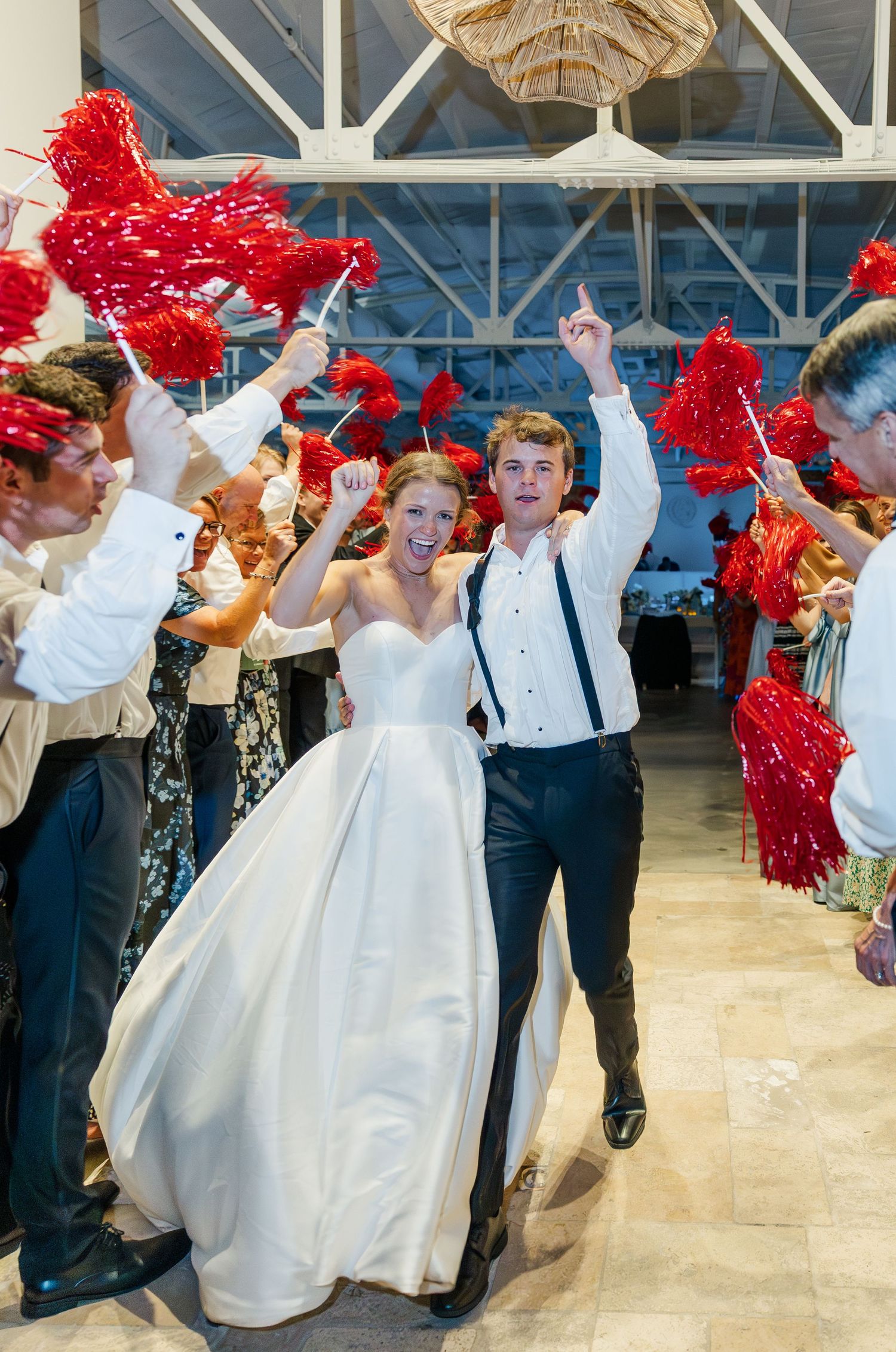 Bride and groom exit reception through red star wand sendoff tunnel with cheering guests.