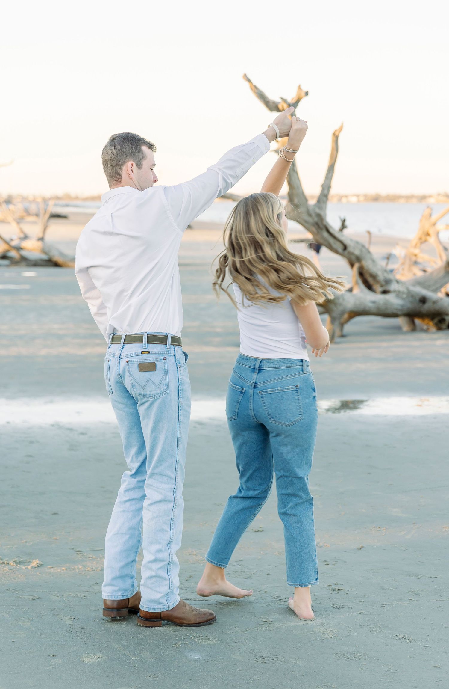 Couple reaching up towards the sky together on a beach at golden hour.