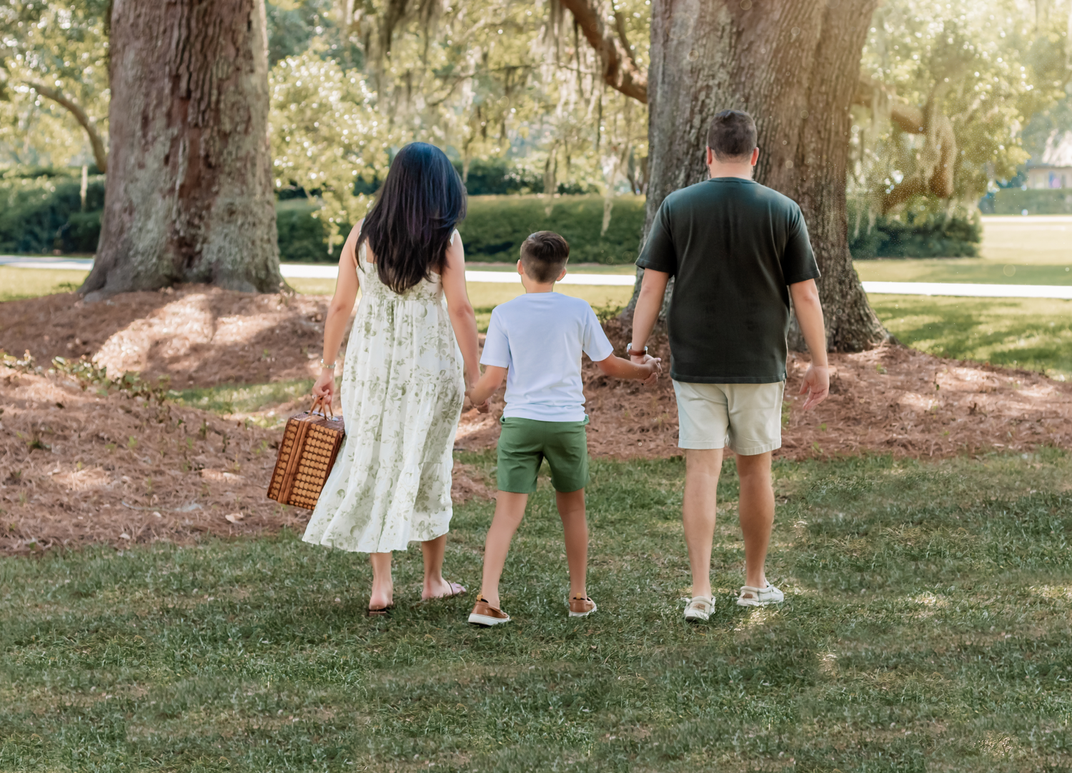 A family holding hands walks through a serene park with Spanish moss hanging from ancient oak trees.