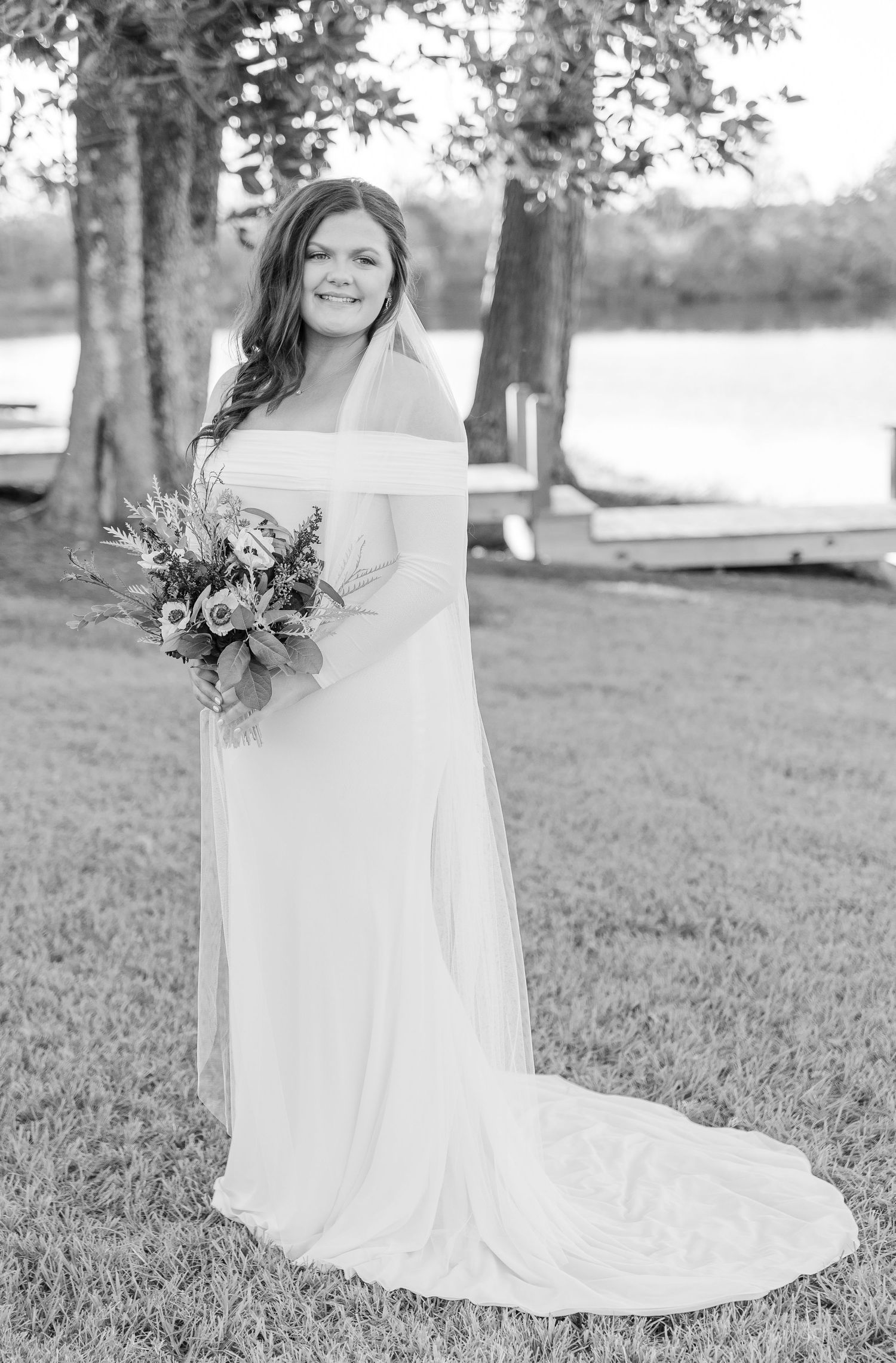 Classic bridal portrait in off-shoulder gown holding bouquet by lakeside setting.