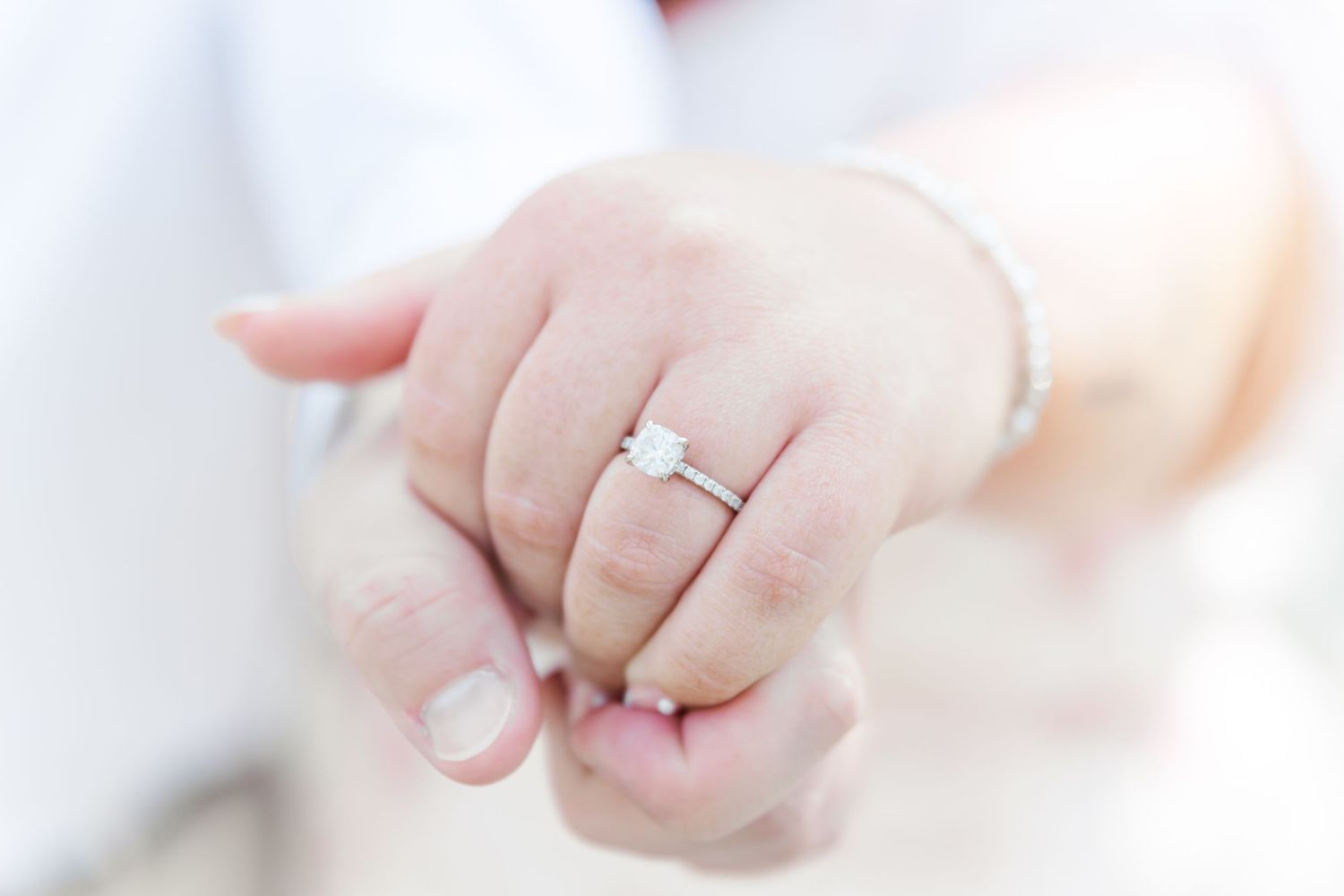 Close-up of an engagement ring on a hand against a soft white background.