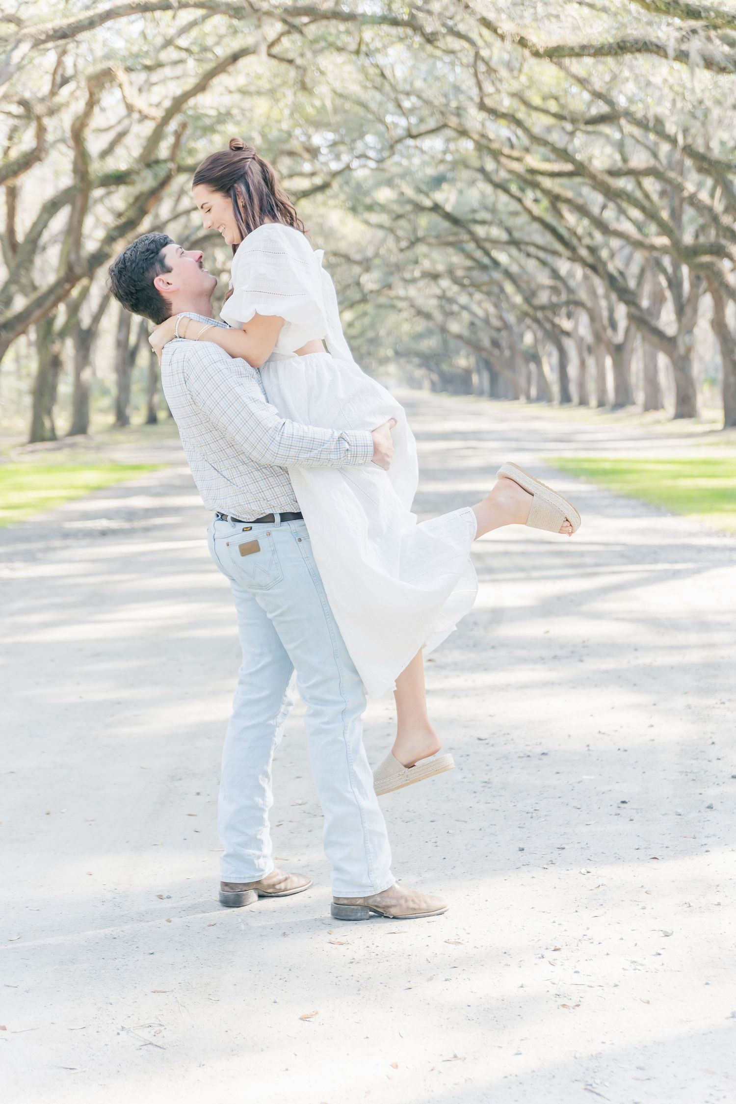 A romantic lift pose captured under a canopy of oak trees on a sunny day.