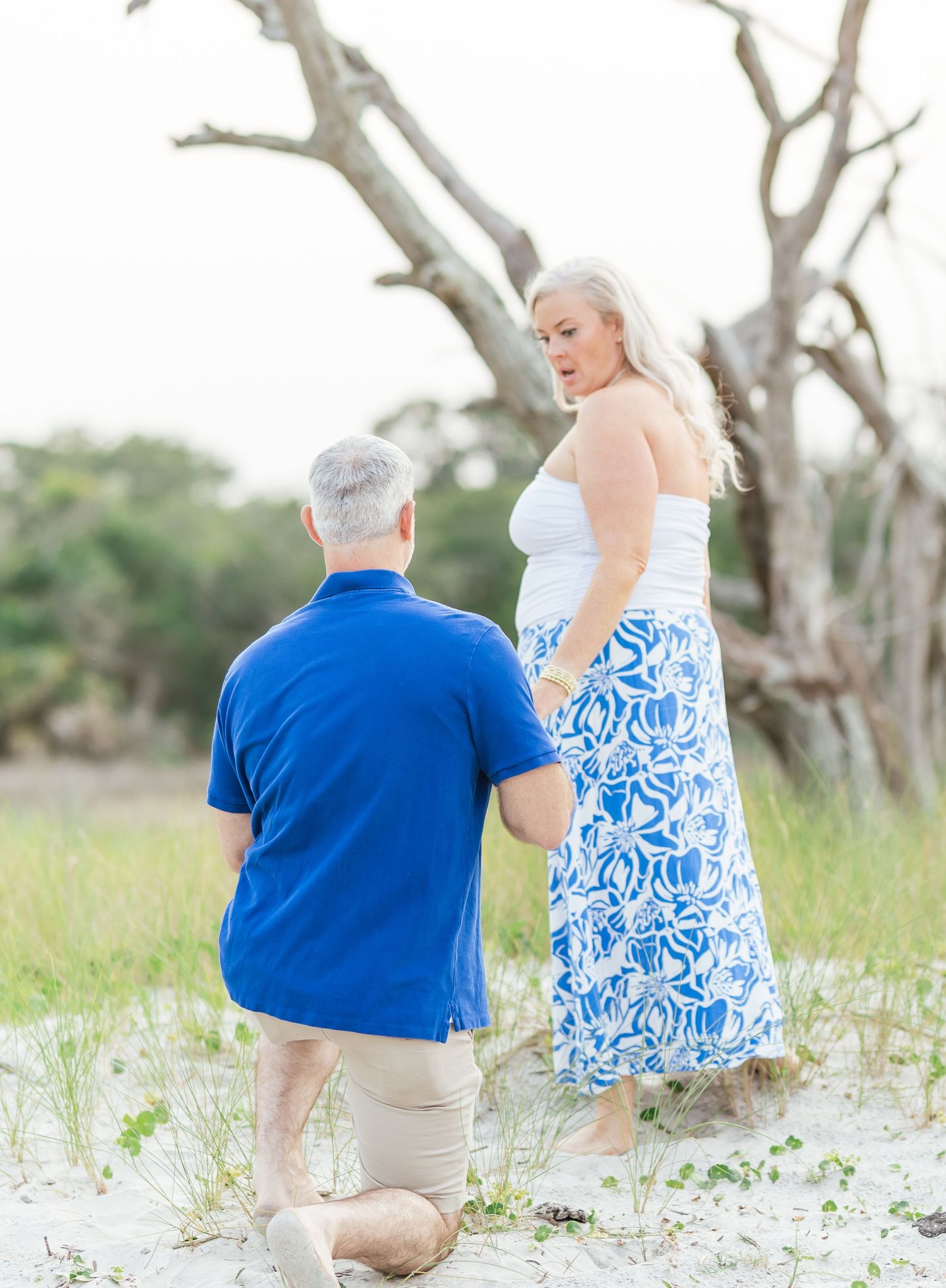 Individuals in coordinating white and blue outfits walk along a sandy beach path with weathered driftwood nearby.