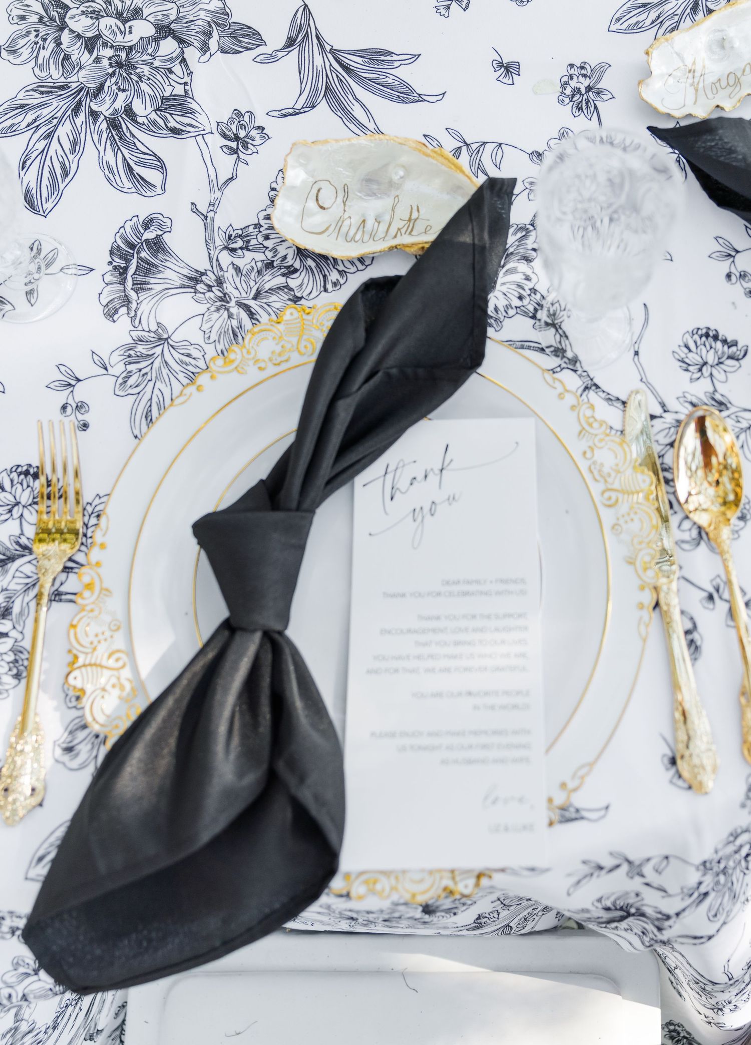 Elegant wedding place setting with blue toile tablecloth, gold flatware, black napkin, acrylic menu card, and geode place card.