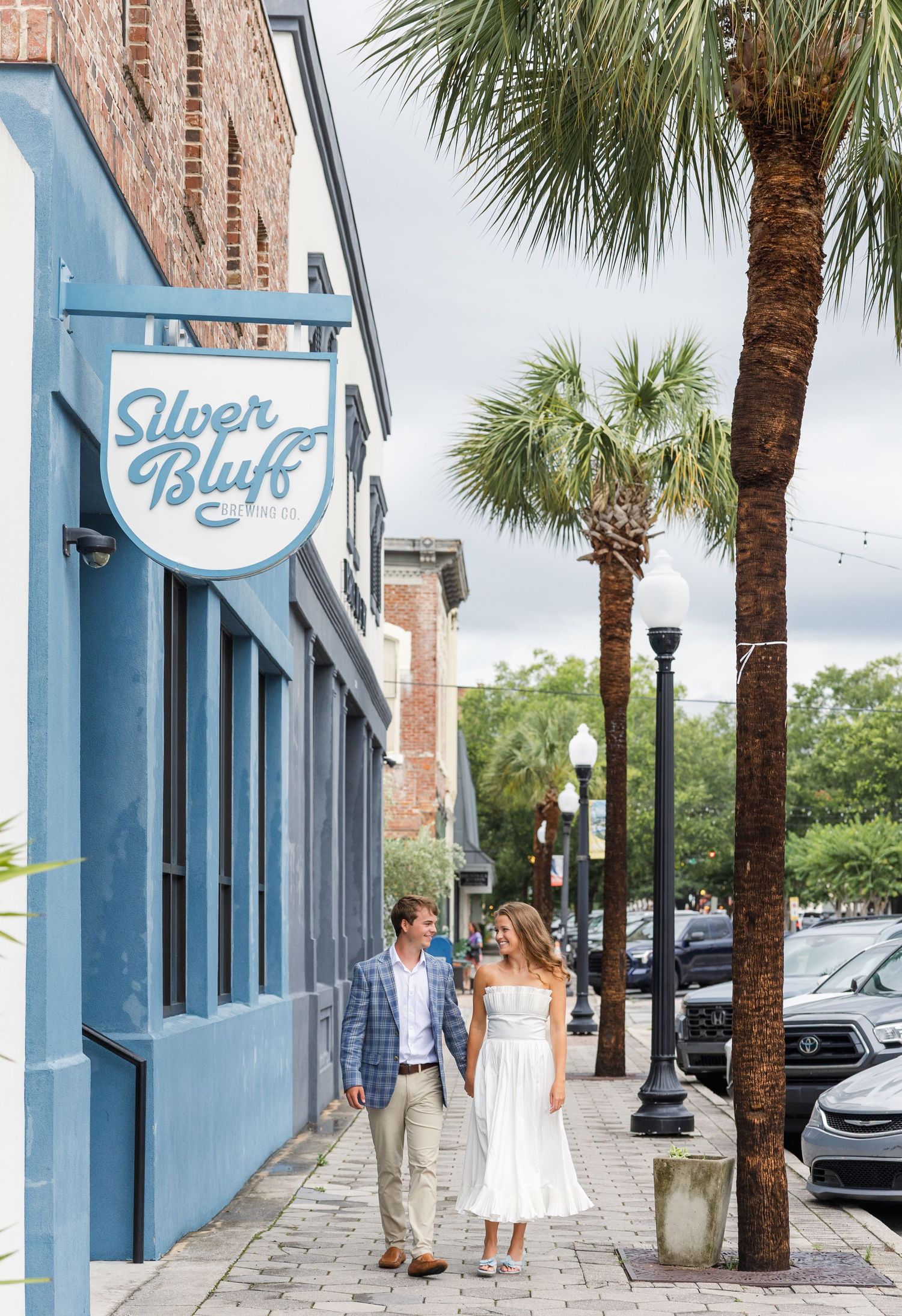 Couple walks hand-in-hand past Silver Bluff bar sign on a charming brick sidewalk.