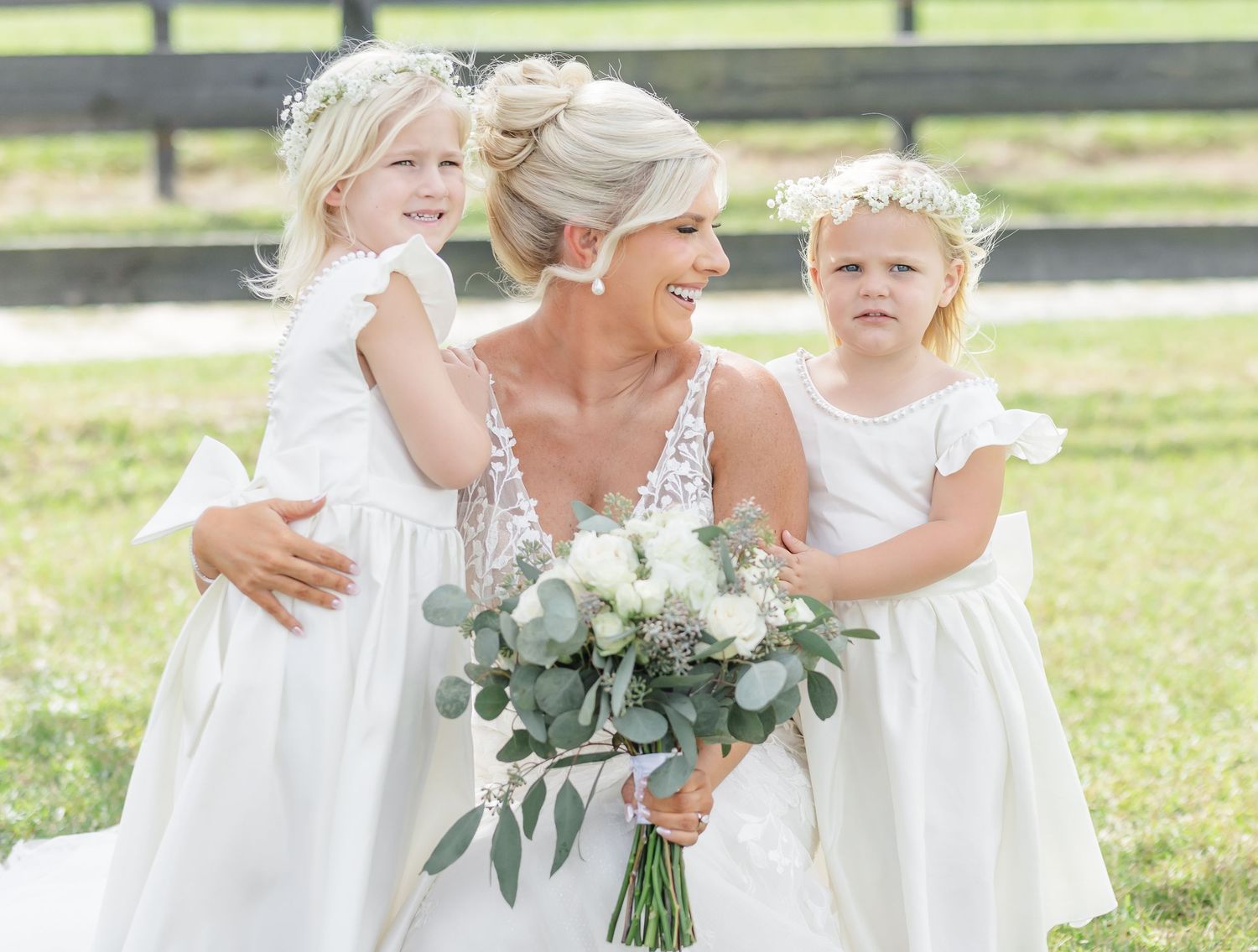 Wedding party members in white dresses gather outdoors holding delicate bouquets with eucalyptus.