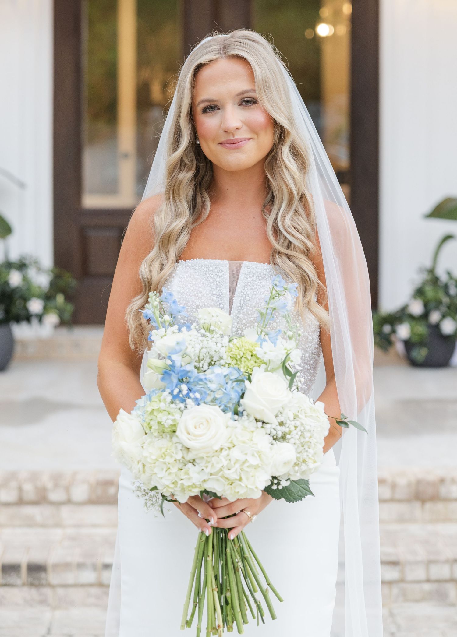 Beautiful blonde bride holding white and blue hydrangea bouquet wearing lace strapless gown and veil.