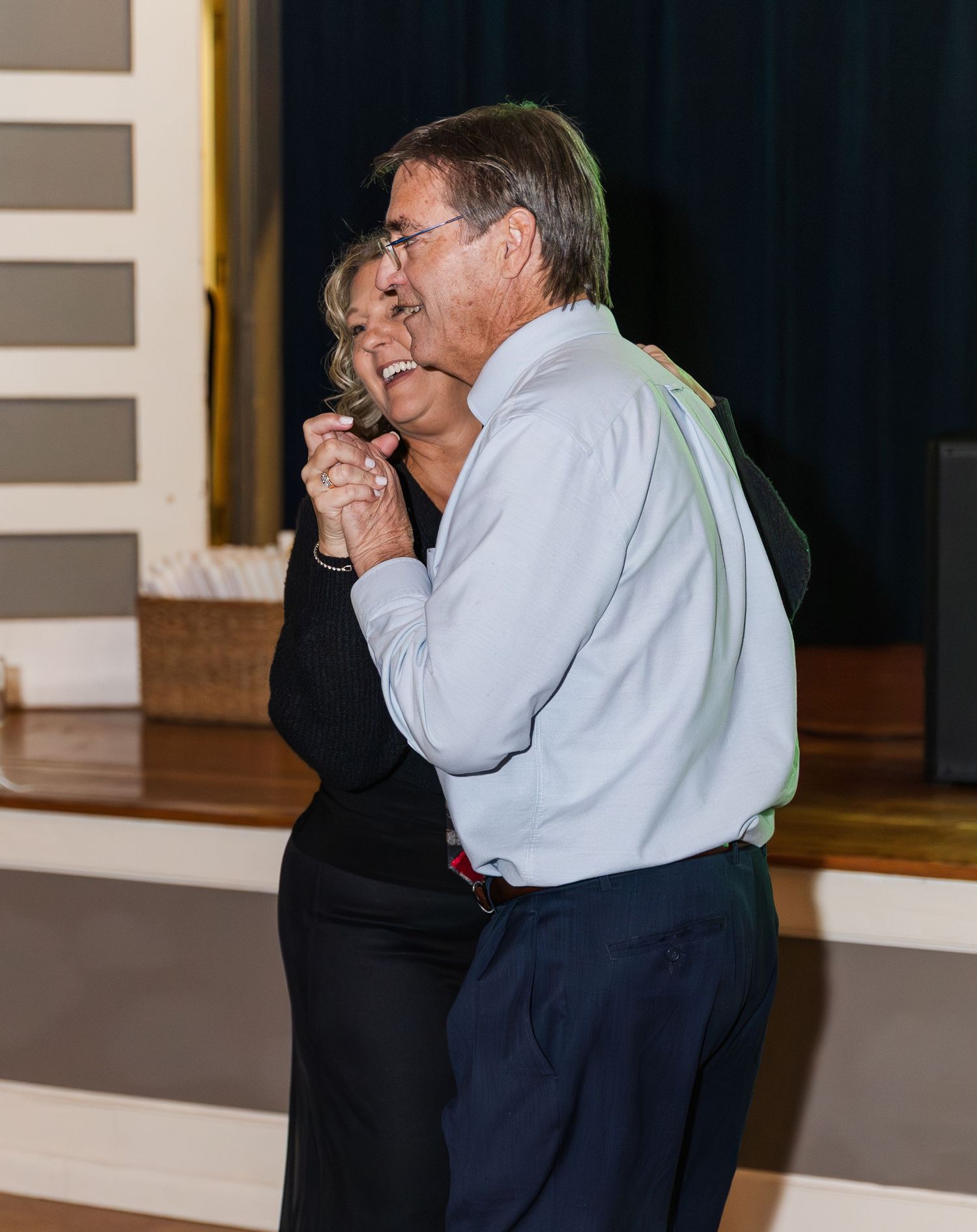 Older couple shares a joyful dance together at a wedding reception, smiling and holding hands.