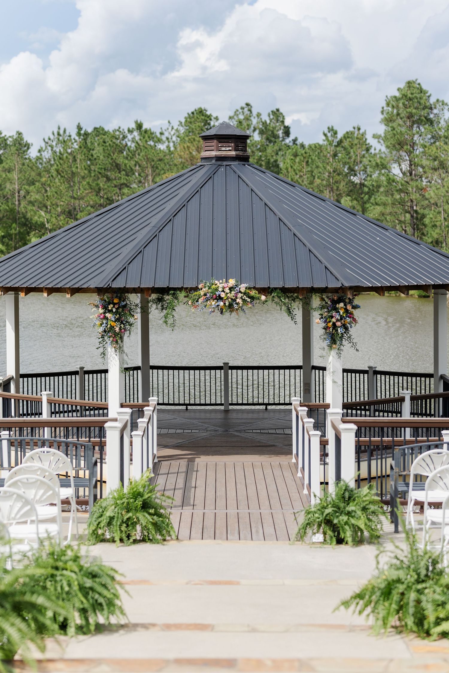Elegant outdoor wedding gazebo with floral arch decorations, white chairs, and lush greenery at a scenic venue.