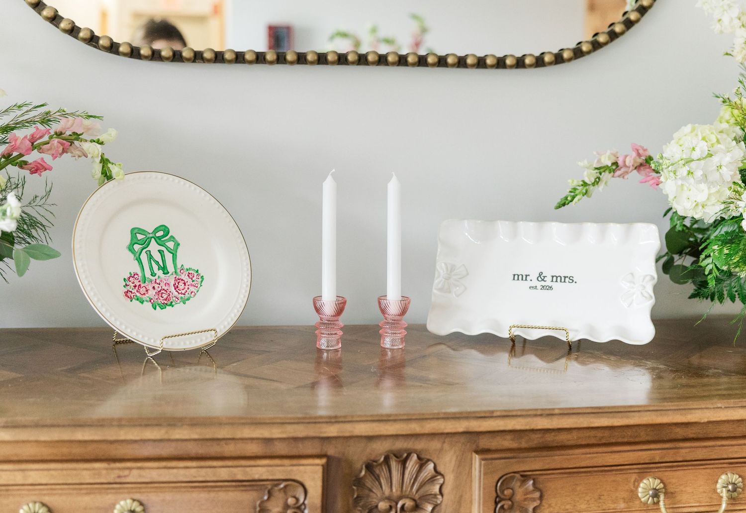 Elegant wedding gift display with Mr. and Mrs. sign, pink candlesticks, and floral decorative plate on wooden dresser.