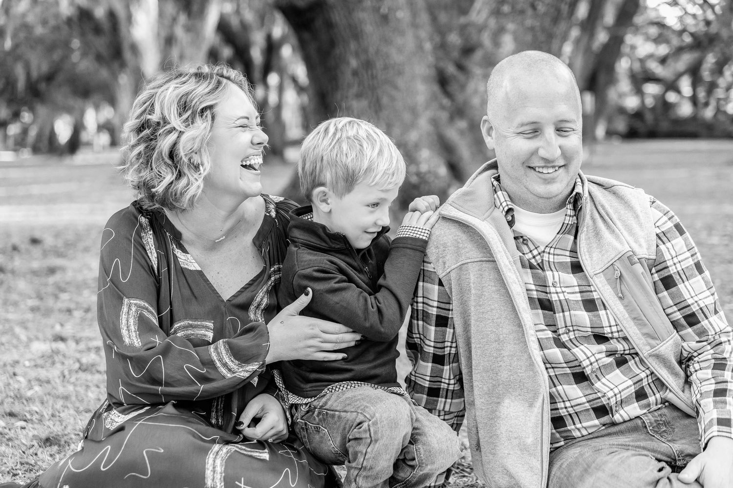 Black and white portrait of family laughing together during outdoor photo session.