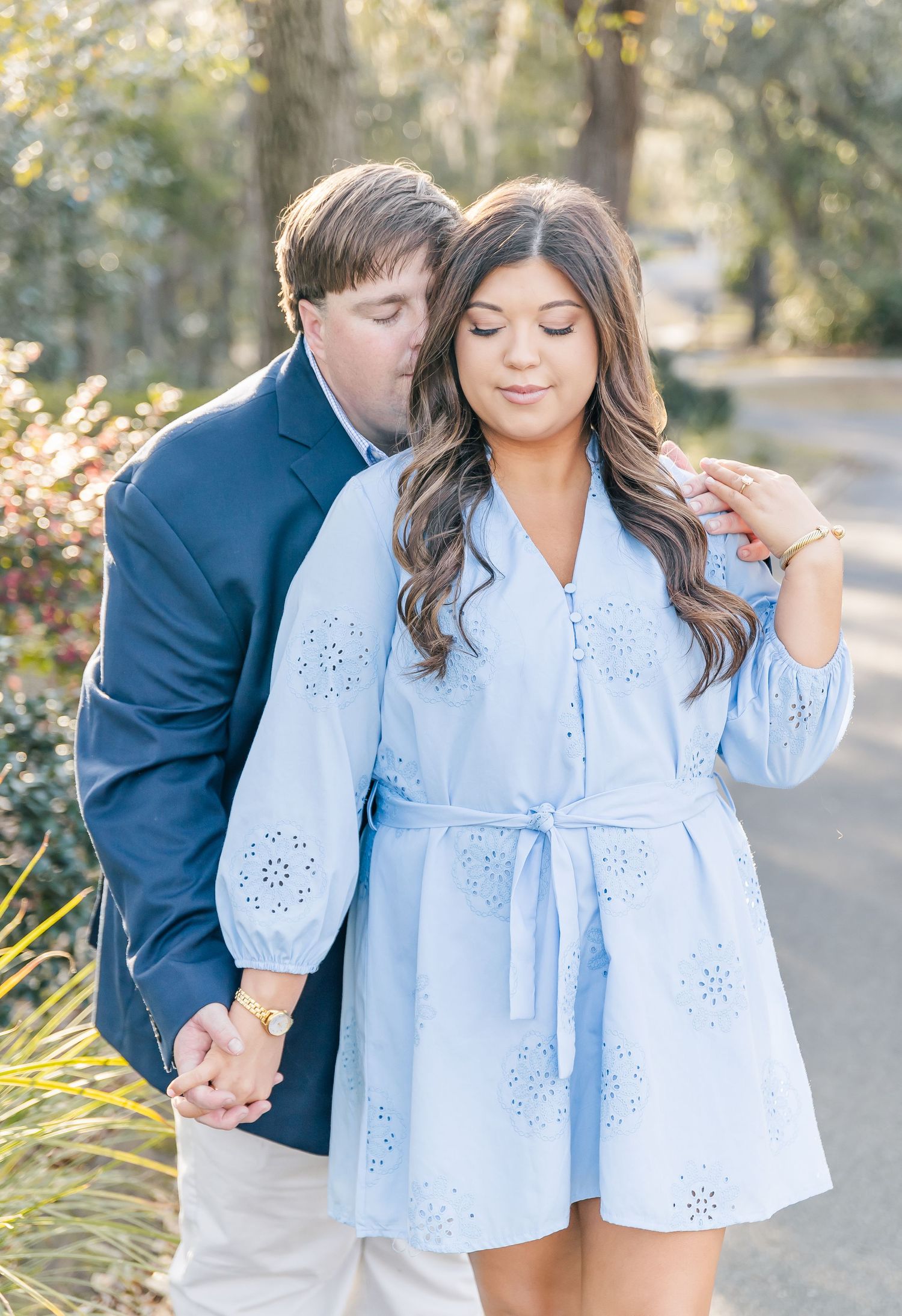 A romantic outdoor portrait of a couple holding hands in coordinated blue and white outfits.
