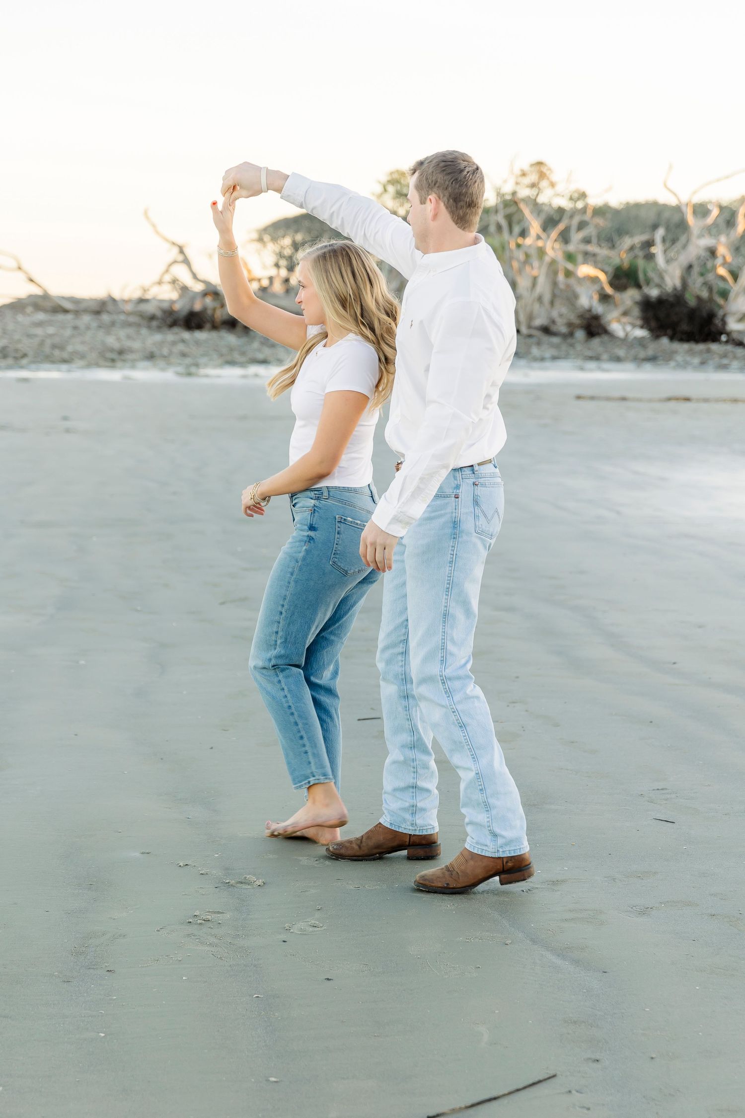 Couple dancing together on a beach wearing coordinated white and denim outfits.