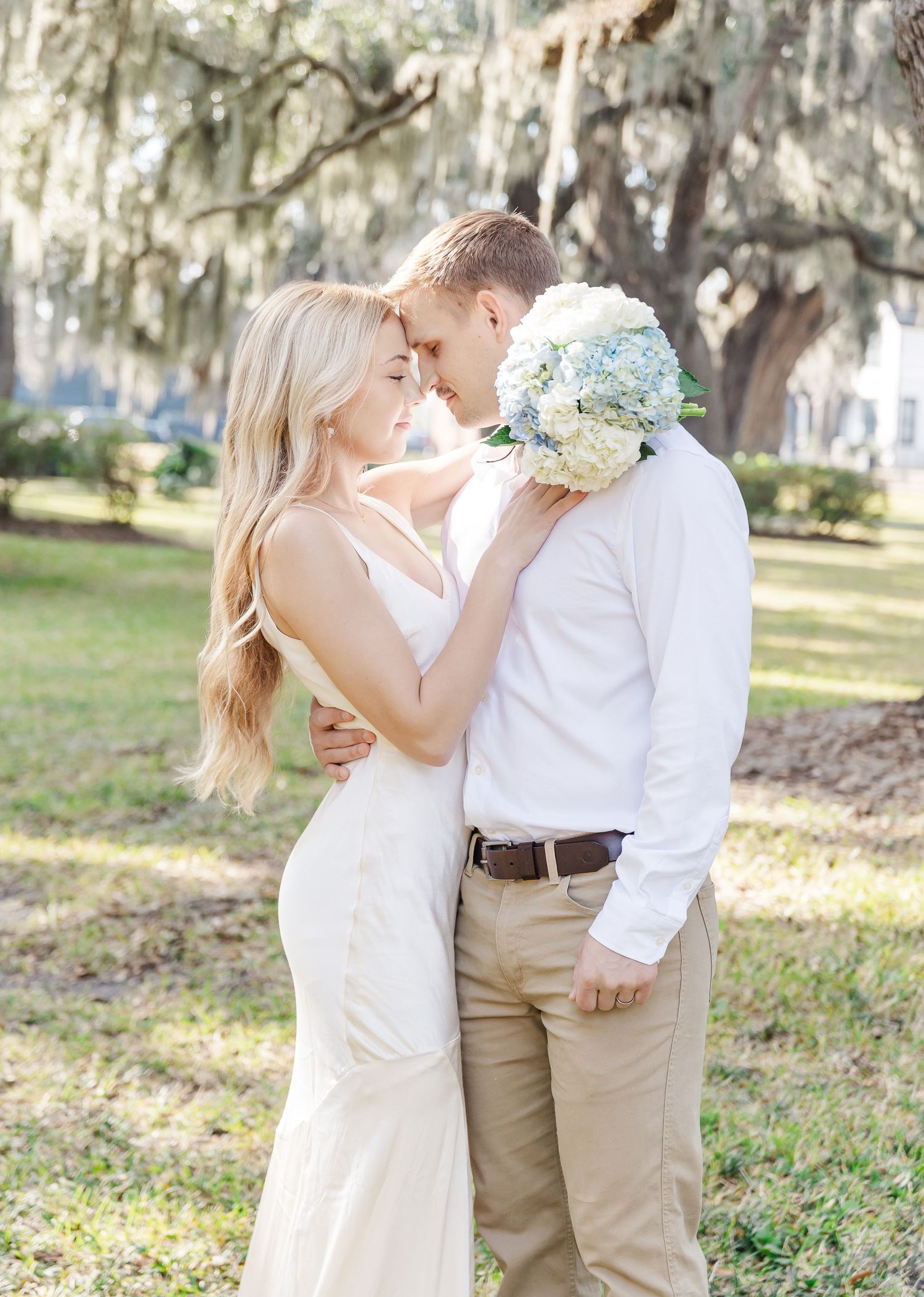 A romantic embrace with blue hydrangea bouquet under Spanish moss covered trees.