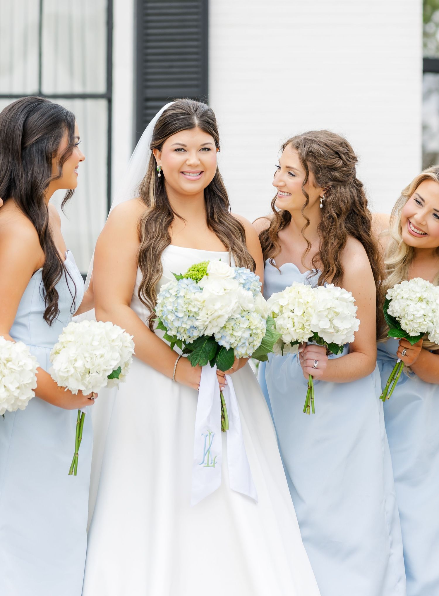 Bride in white gown holds hydrangea bouquet surrounded by bridesmaids in light blue dresses.