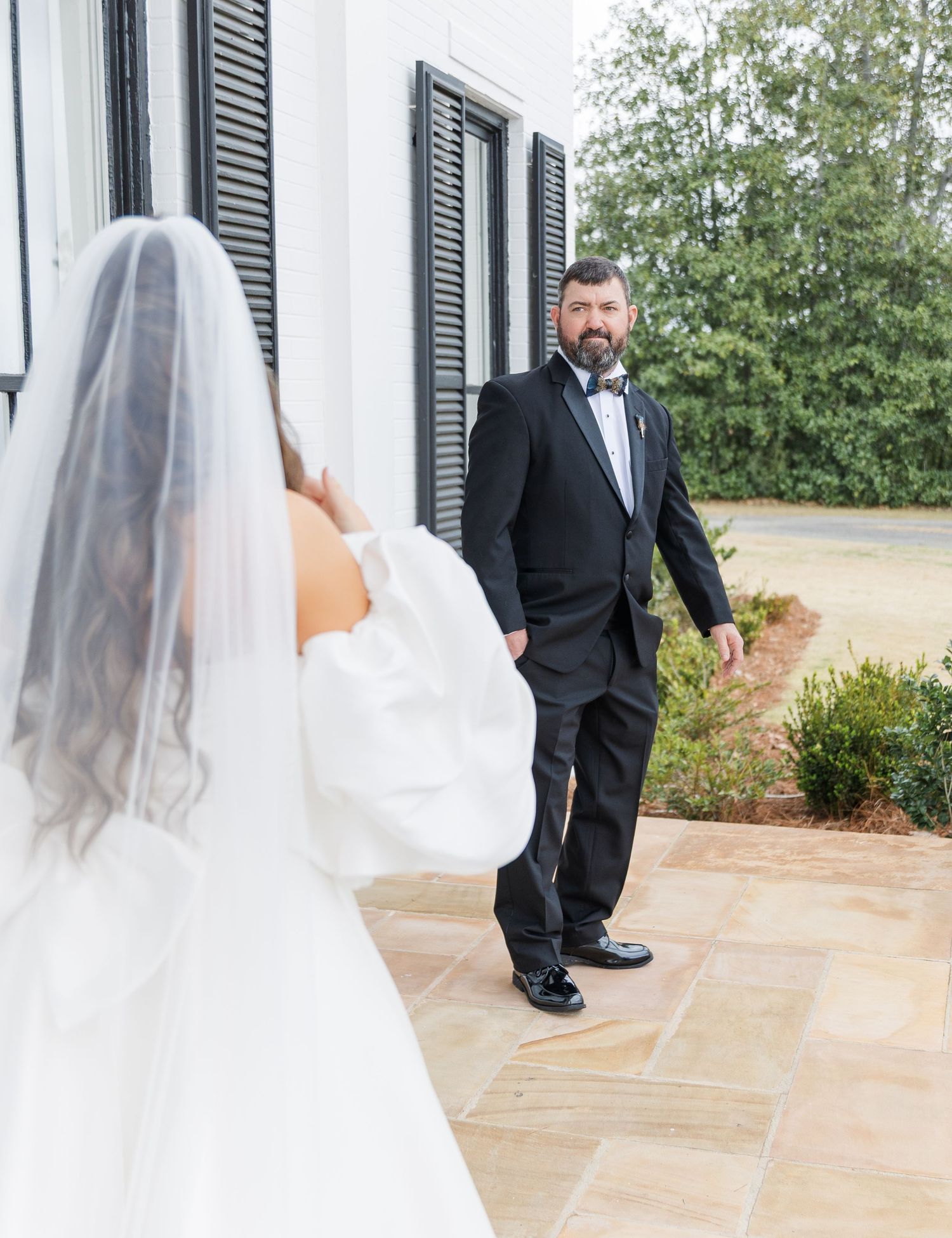 Emotional first look moment as groom in black tuxedo turns to see bride in white wedding gown.