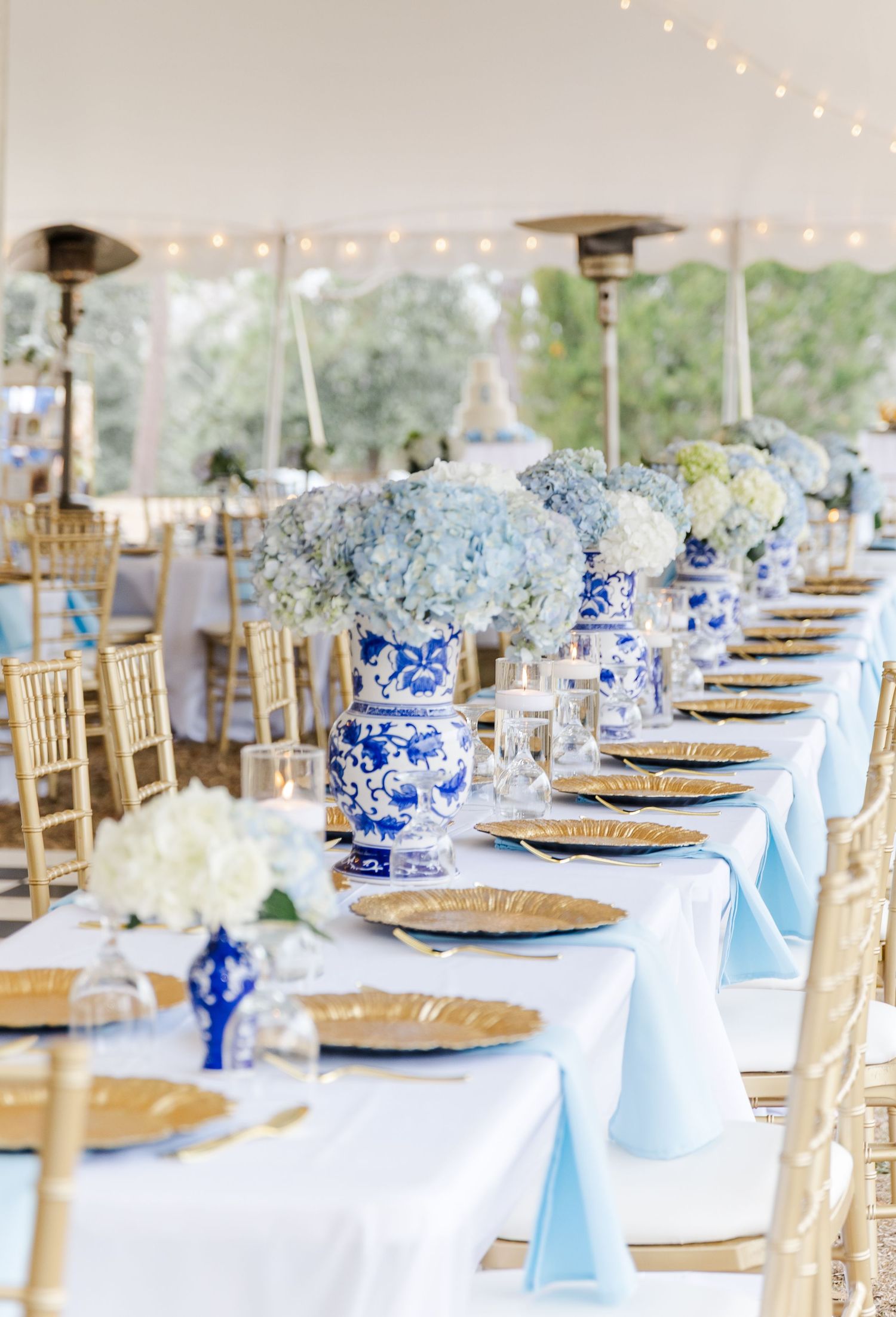 Elegant wedding reception table with blue and white chinoiserie vases, hydrangeas, gold chargers, and light blue napkins.