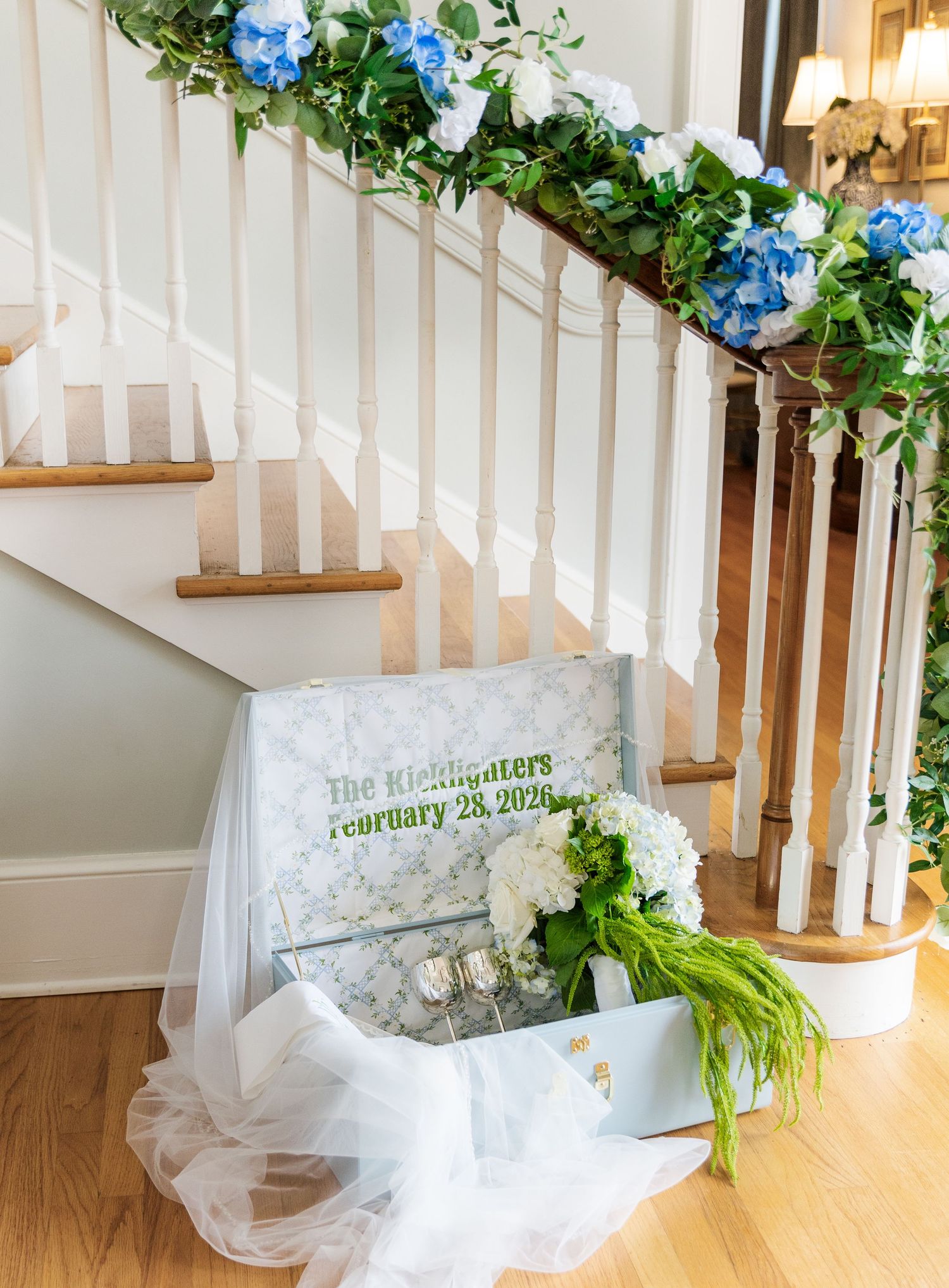 Wedding staircase decorated with blue hydrangeas and greenery garland, with a personalized couples sign and bridal veil.