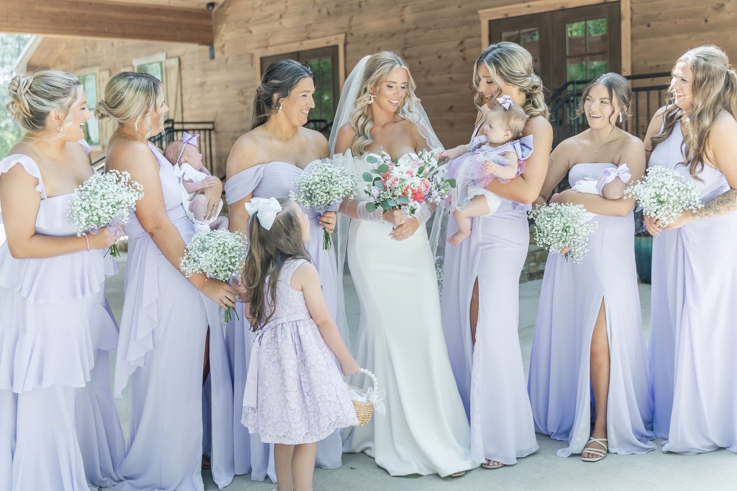 Bridesmaids in flowing lavender gowns hold baby's breath bouquets while standing with bride.