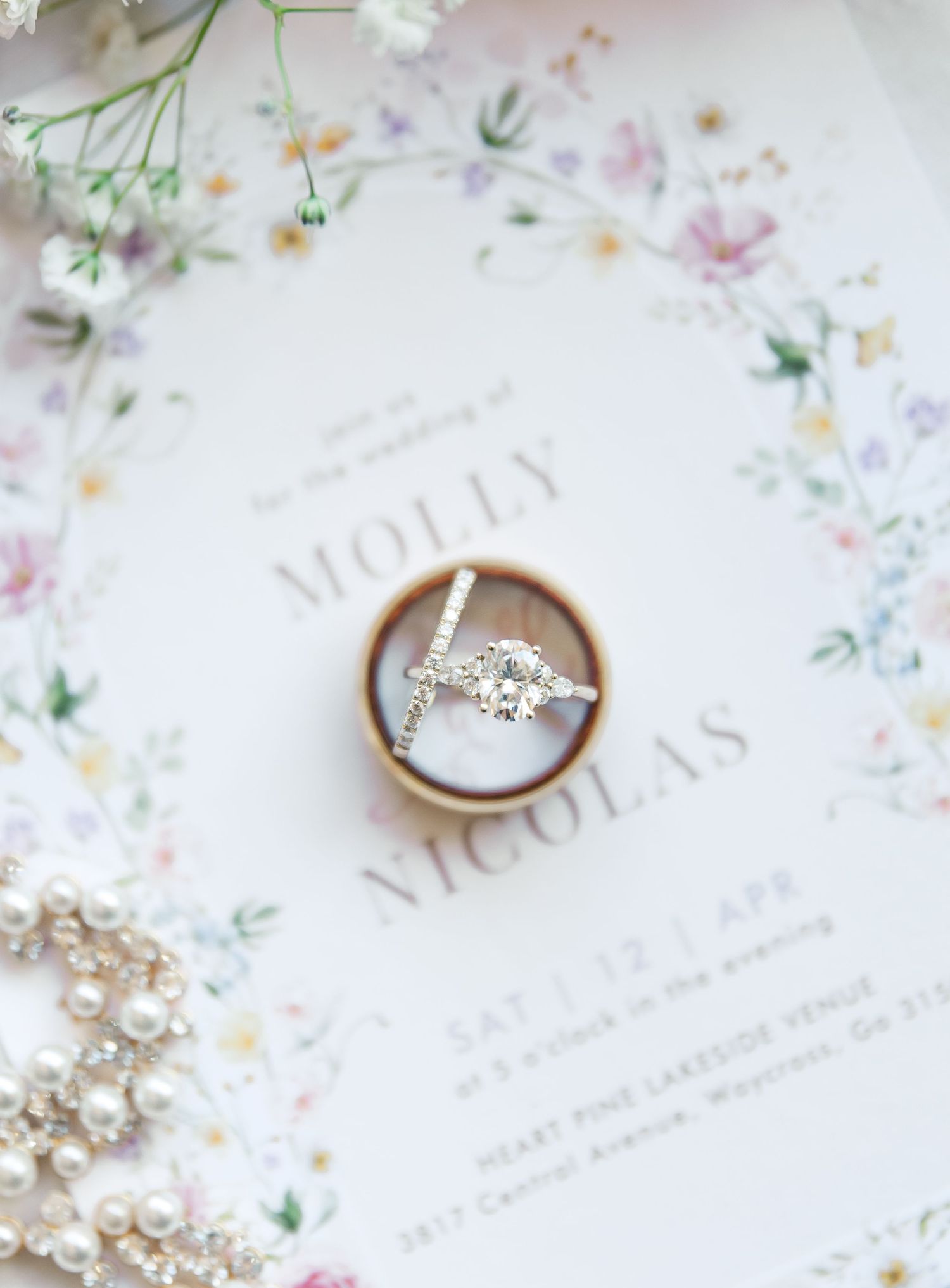 Diamond engagement ring photographed on floral wedding invitation with pearl jewelry.