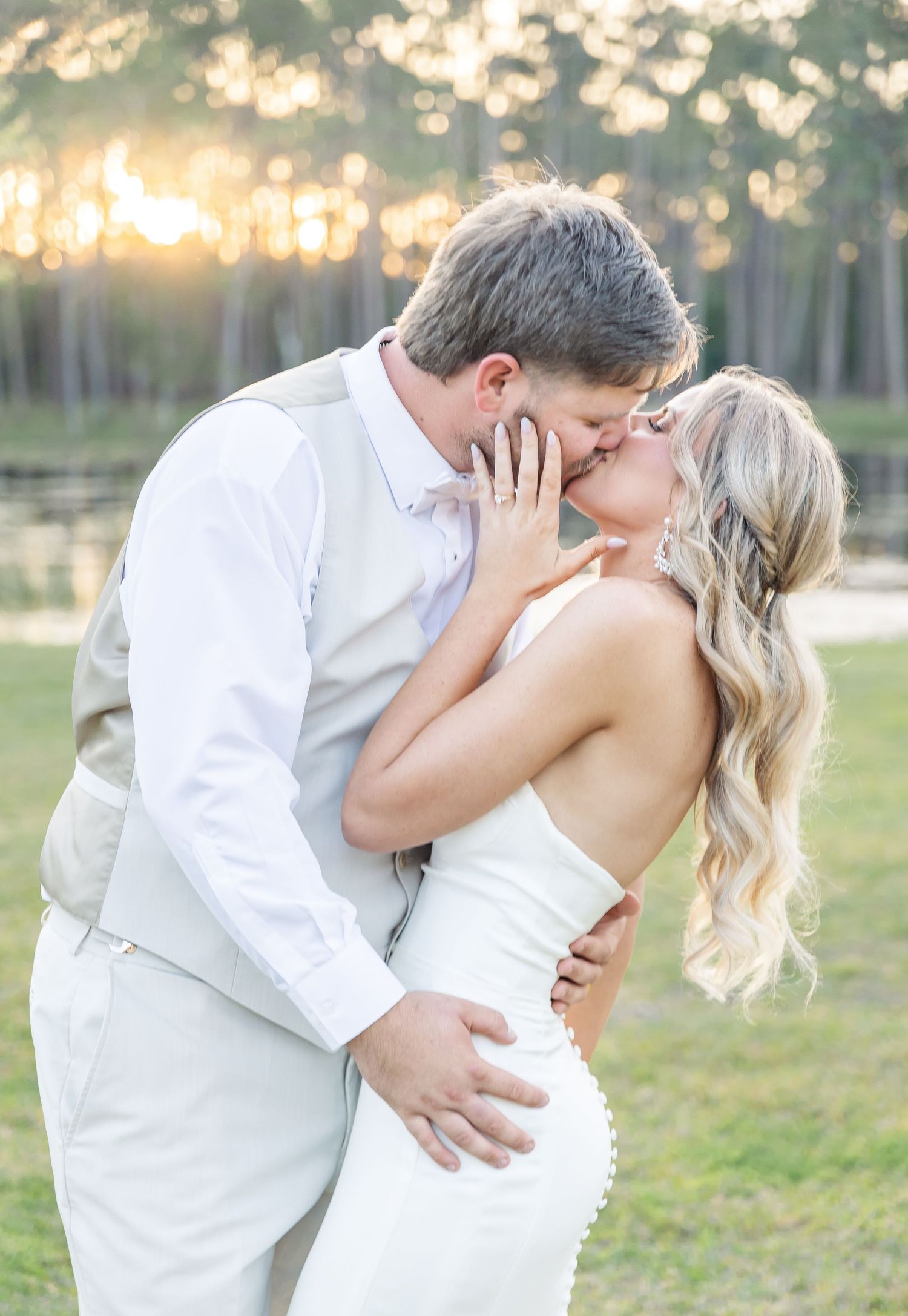 Romantic wedding moment captured as couple shares passionate kiss outdoors at sunset.