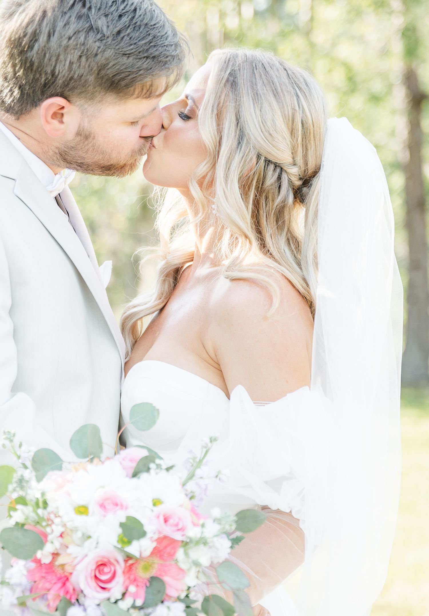 An intimate wedding portrait of a couple kissing while holding a pink rose bouquet.
